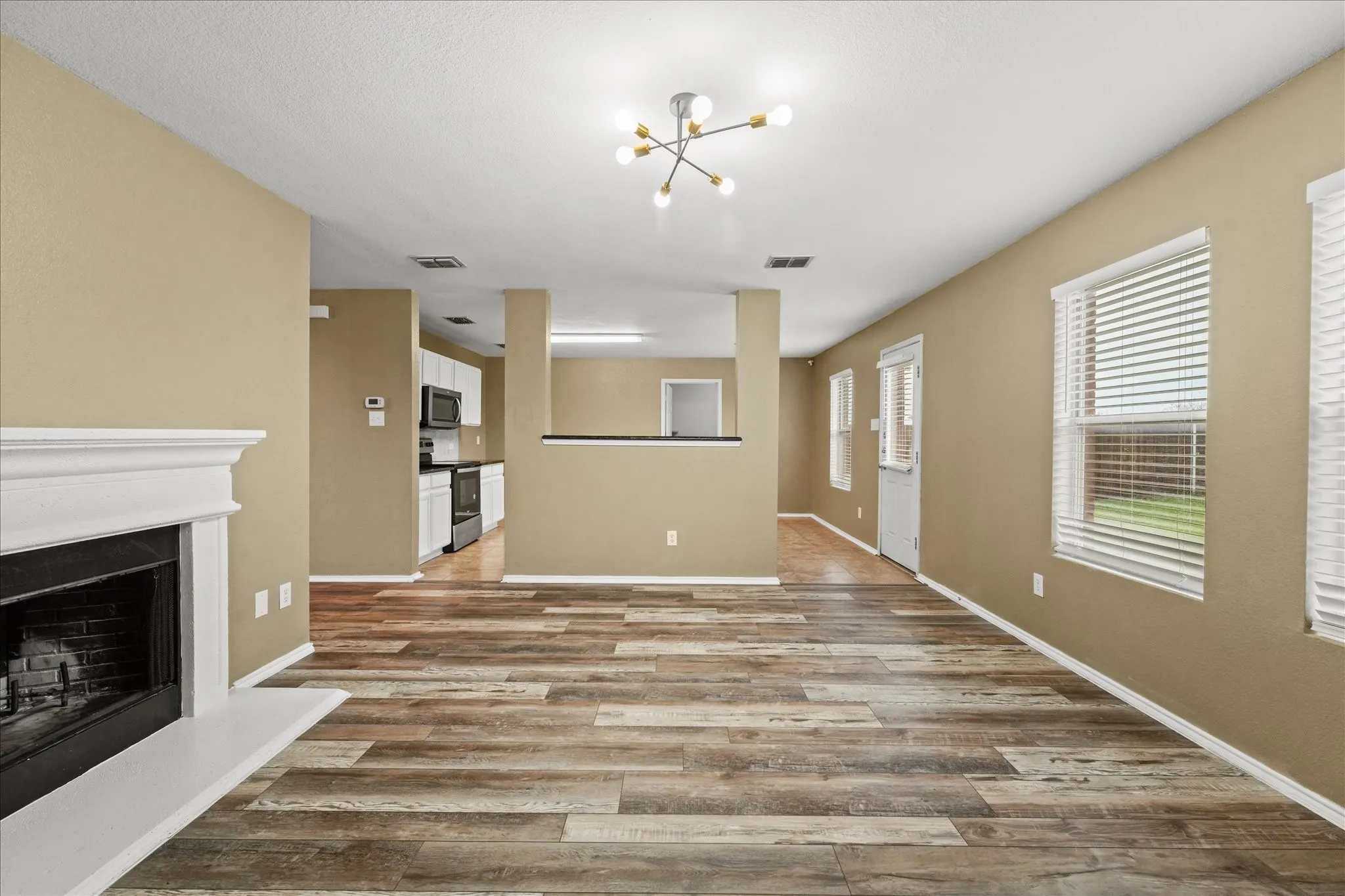 Unfurnished living room with a chandelier, wood finished floors, and a fireplace with raised hearth