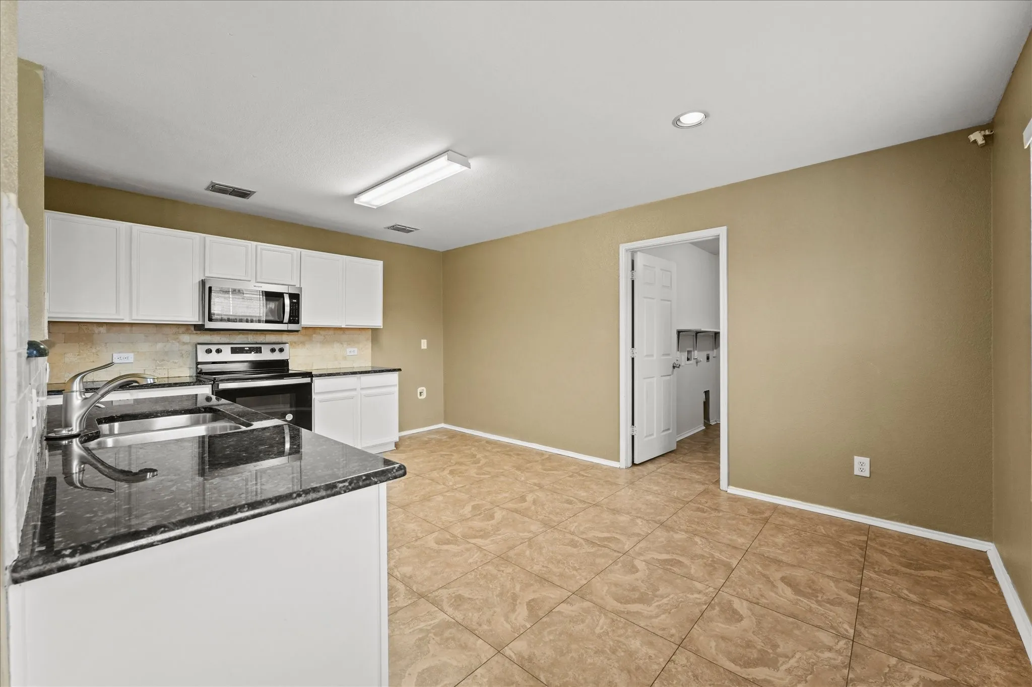 Kitchen featuring stainless steel appliances, dark stone countertops, white cabinets, decorative backsplash, and light tile patterned floors