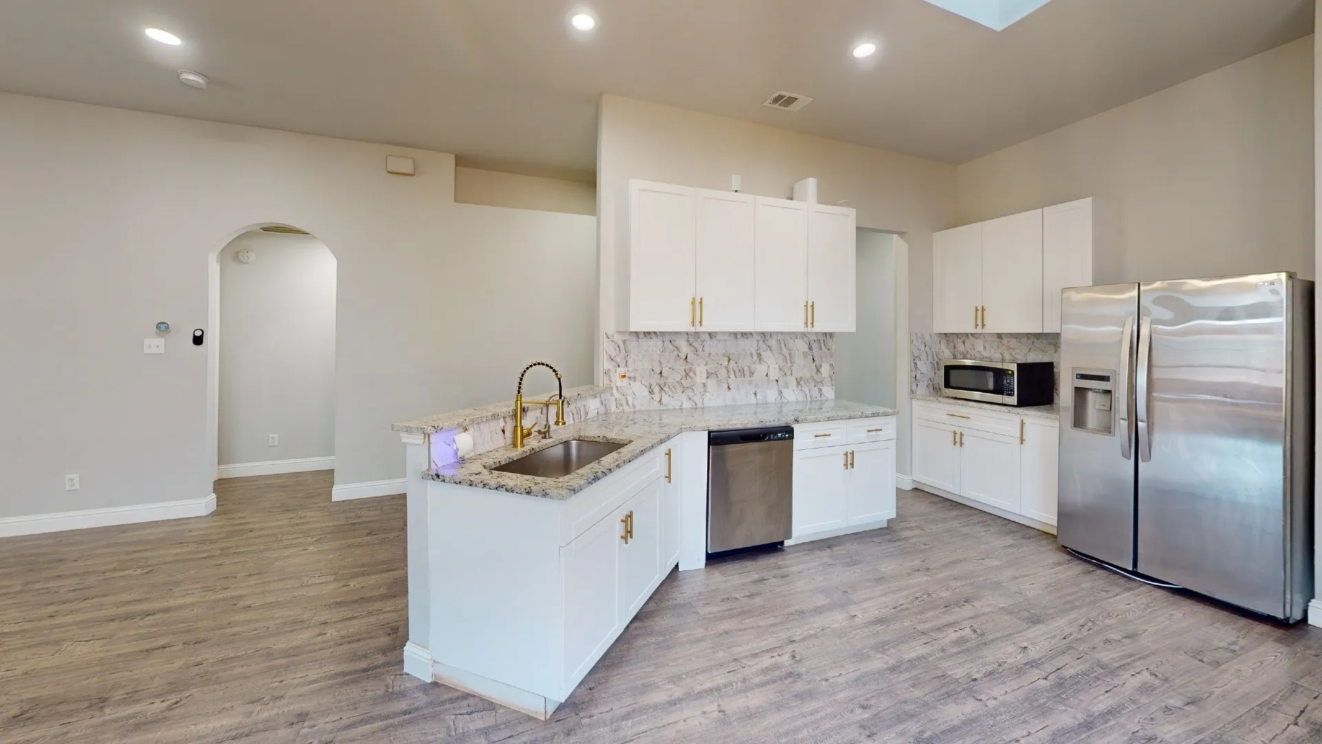 Modern kitchen featuring white cabinetry, gold-tone hardware, and a stone-finish backsplash