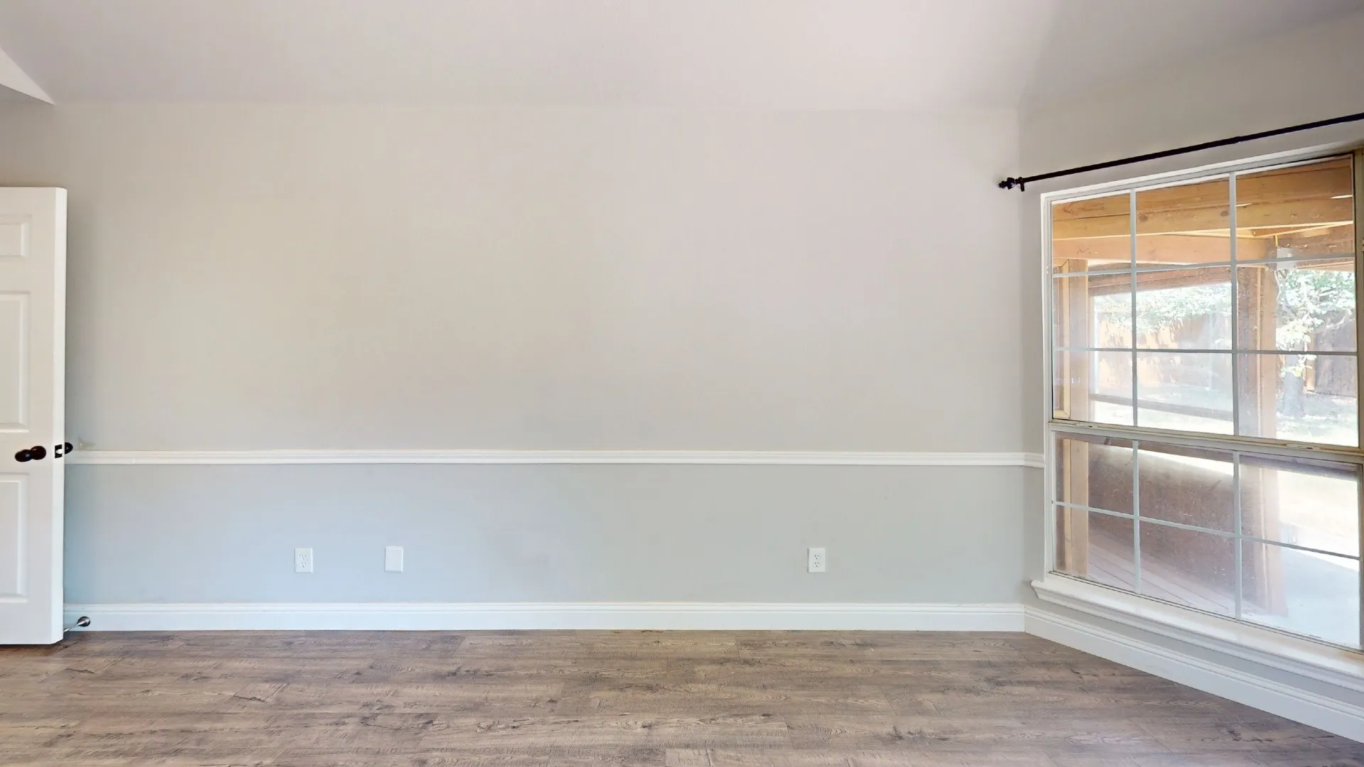 Spacious living area featuring wood-finish flooring, neutral two-tone wall treatment with chair rail detail, and abundant natural light from large windows with wood blinds