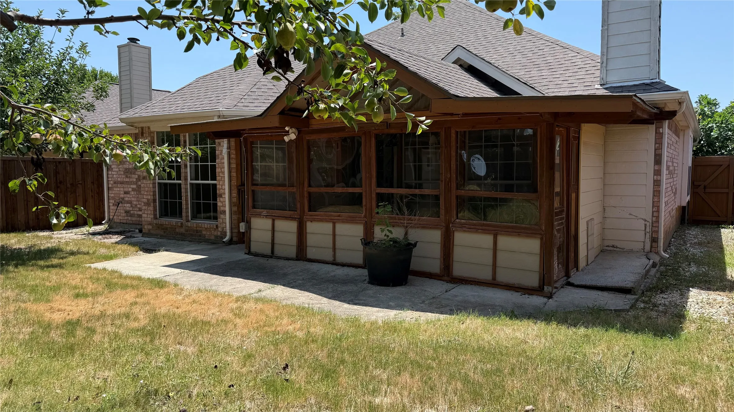 Expansive outdoor space featuring a covered patio, a sunroom with wood-frame windows, and a brick exterior