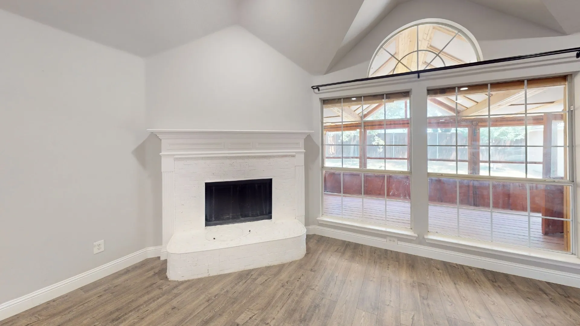 Living area featuring a painted brick fireplace with a mantel, vaulted ceiling, and wood-finish flooring