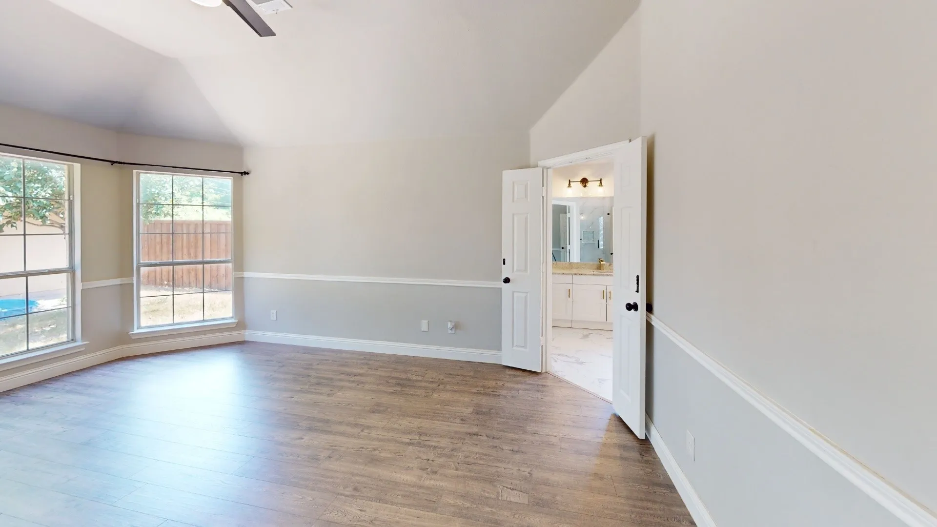 Spacious room featuring vaulted ceilings, wood-finish flooring, and abundant natural light from dual glass doors and windows