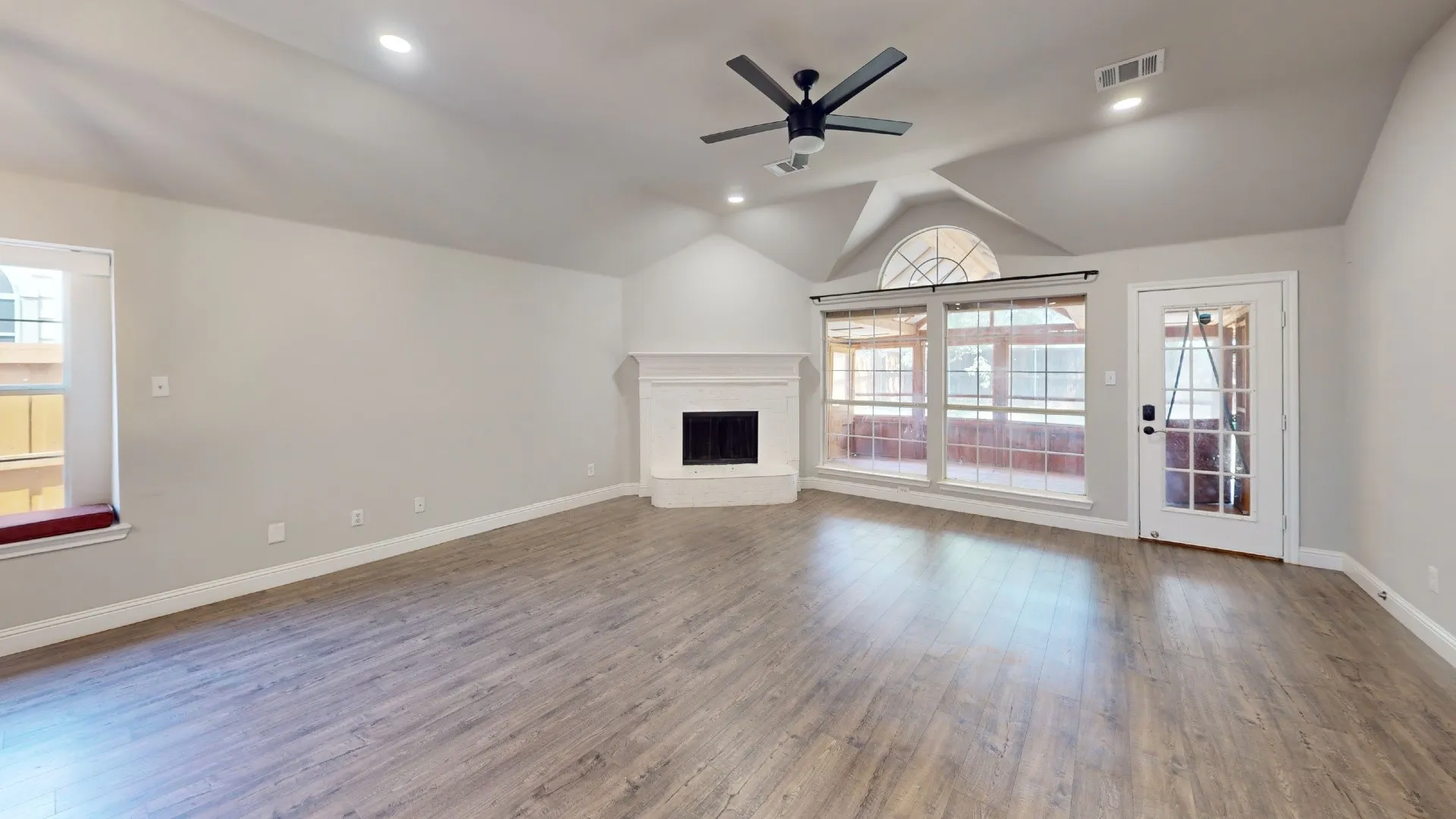 Spacious open-concept great room showcasing gleaming wood-finish flooring, vaulted ceiling with architectural detail, and a modern ceiling fan