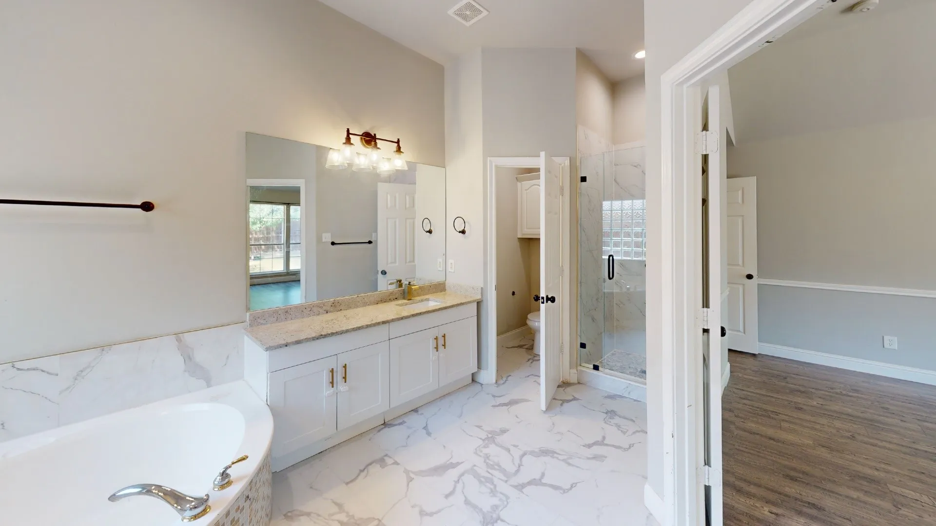Spacious bathroom featuring a large soaking tub with tile surround, a double vanity with stone countertop and ample storage, an enclosed shower with glass doors, and elegant tile flooring