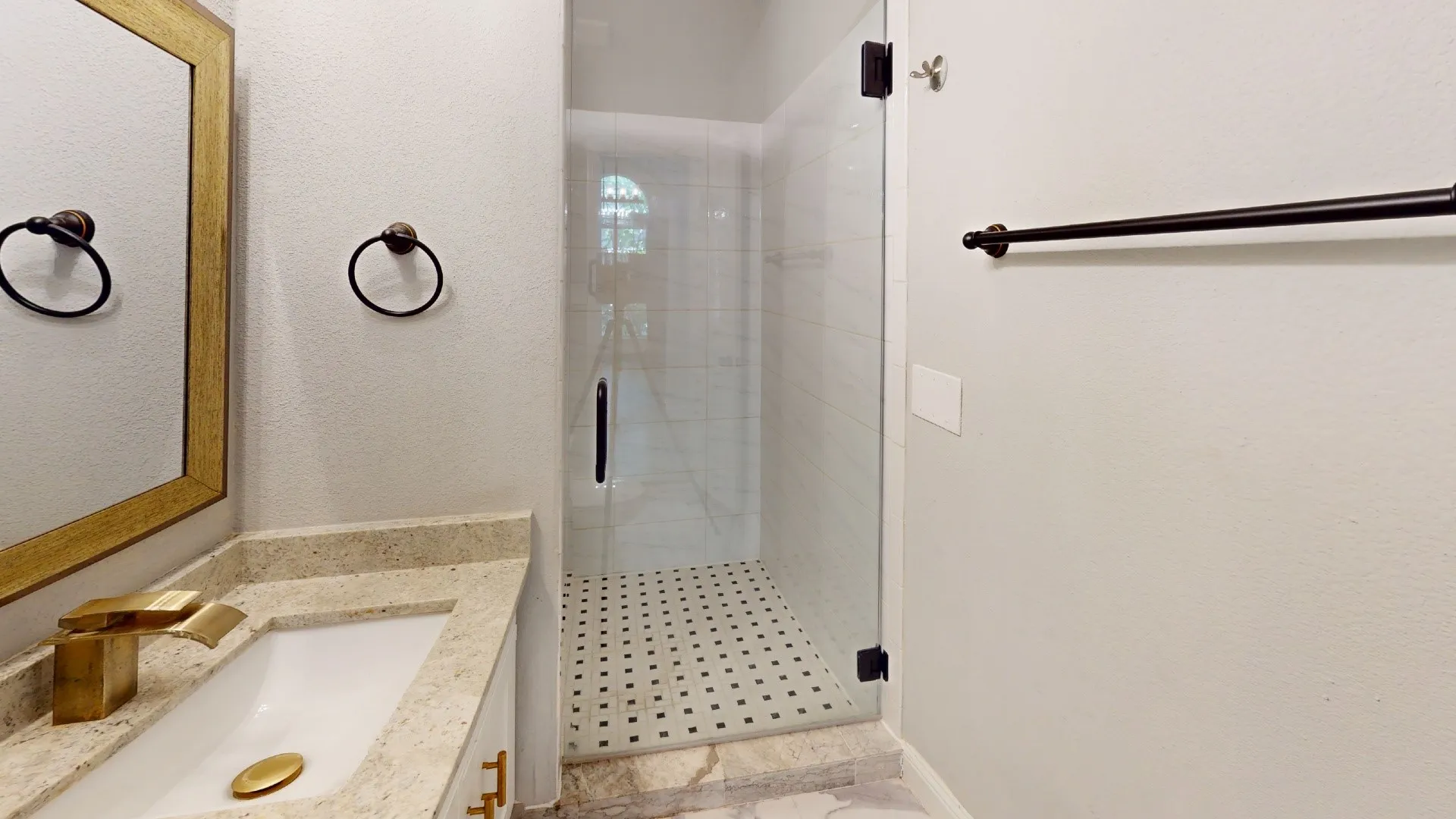 Modern bathroom featuring a walk-in shower with clear glass enclosure, white subway tile walls, and a black and white mosaic tile floor