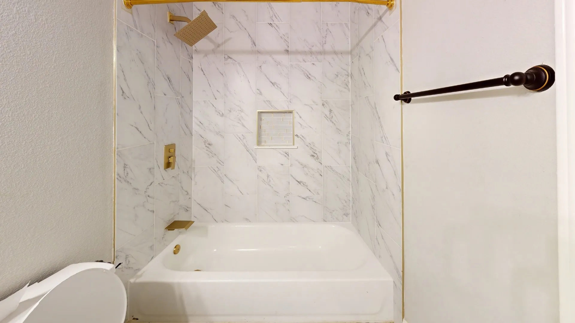Bathtub with white subway tile surround, gold-finish fixtures, and a recessed shower niche