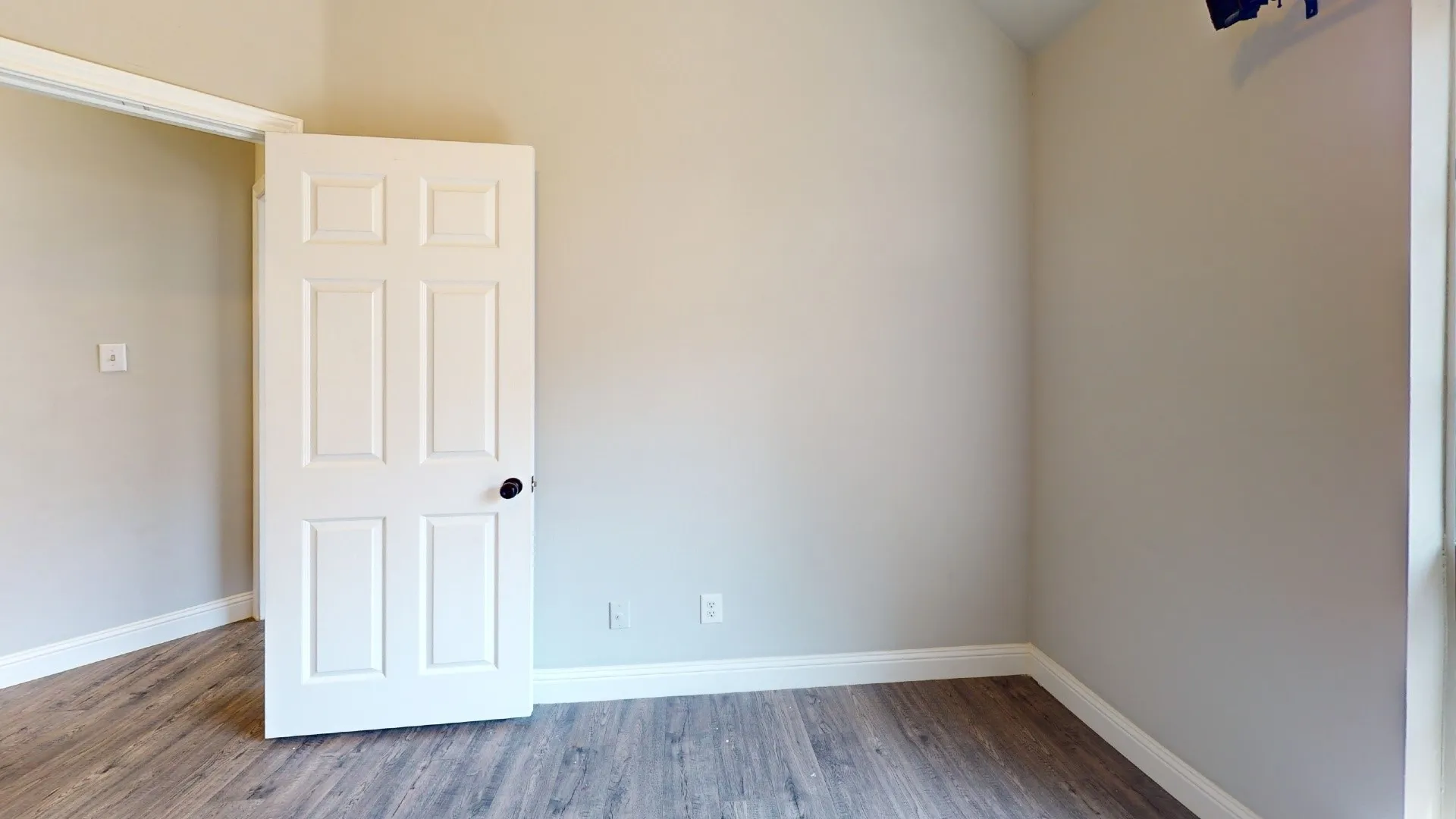 Bright secondary bedroom featuring neutral wall finishes, wood-finish flooring throughout, and a six-panel closet door with polished hardware