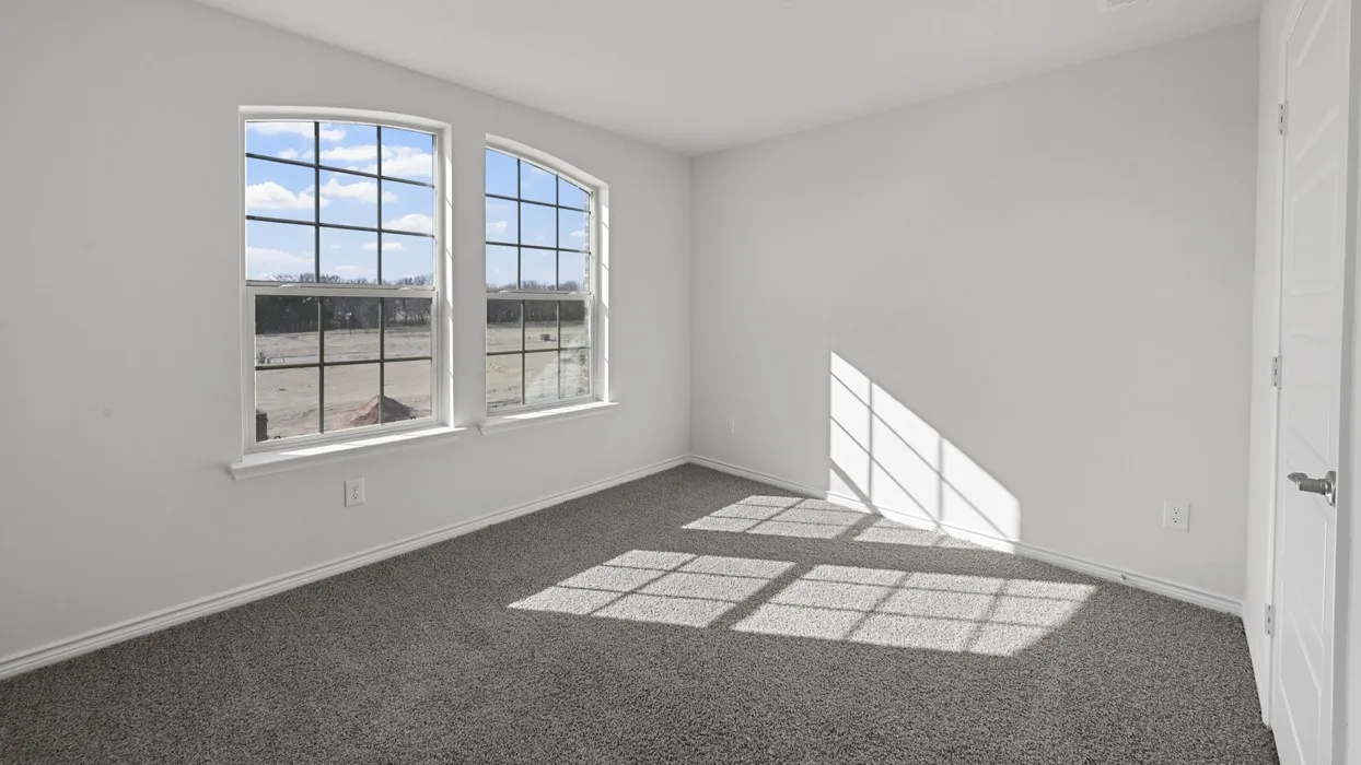 Bright room featuring two arched windows with grid patterns, light gray carpet, white walls, and a modern white paneled door with a brushed nickel handle