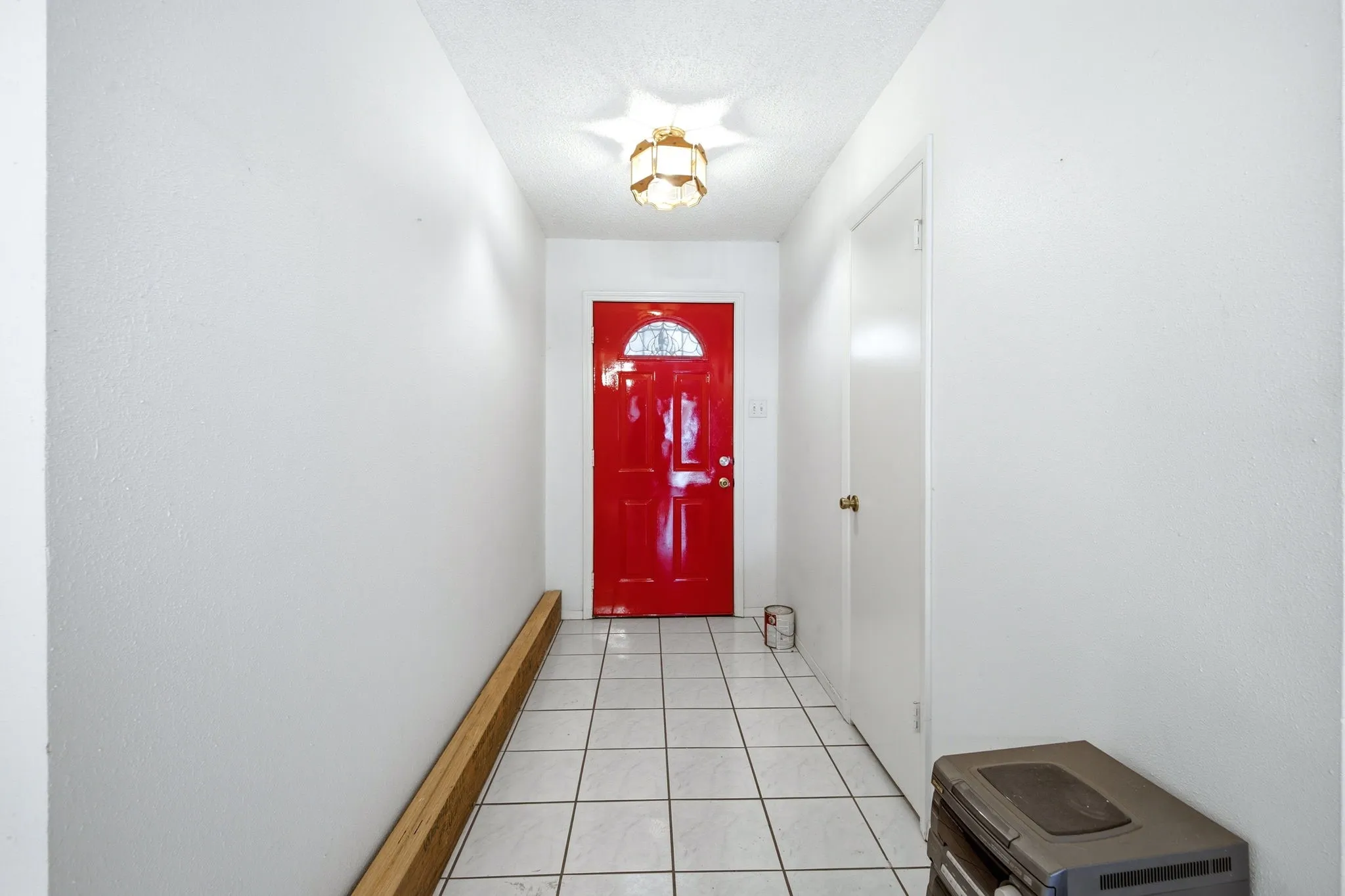 Interior entry hallway with tiled flooring, neutral walls, bench seating, and a bold red front door.