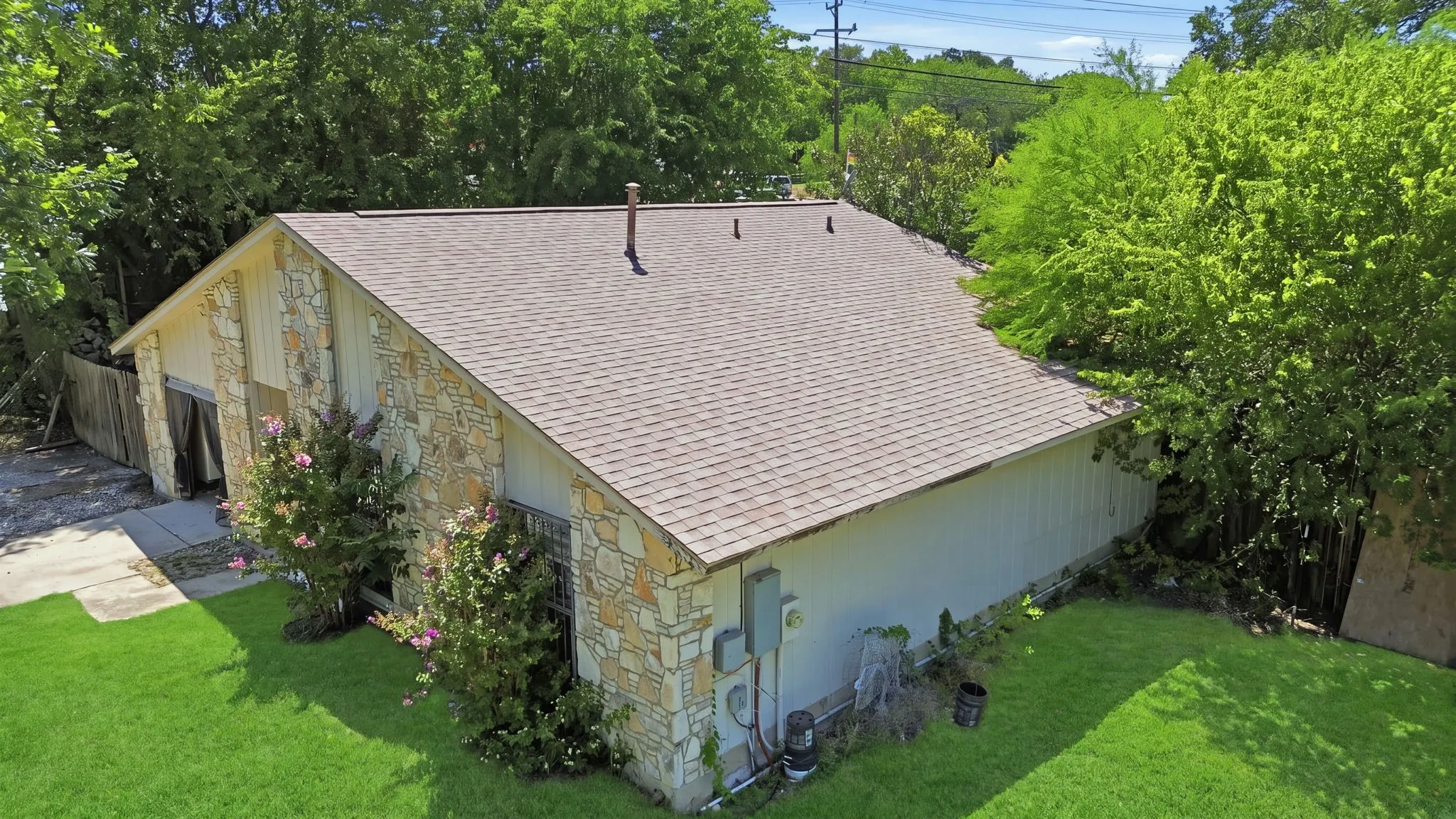Elevated aerial view of the stone home highlighting the shingle roof, surrounding trees, and yard.