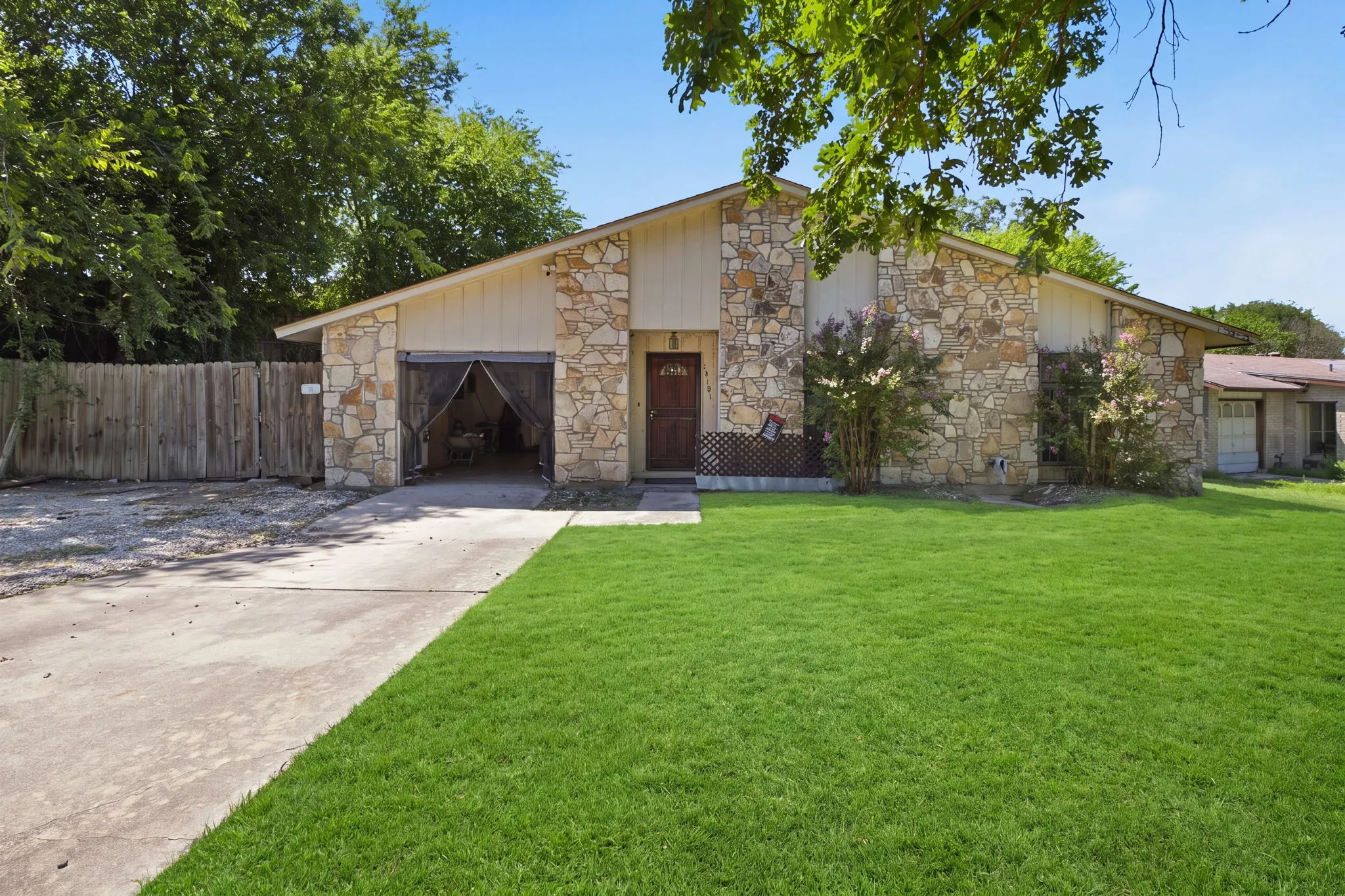 Angle shot of the stone home facade, long paved driveway, and bright green lawn under bright blue skies.