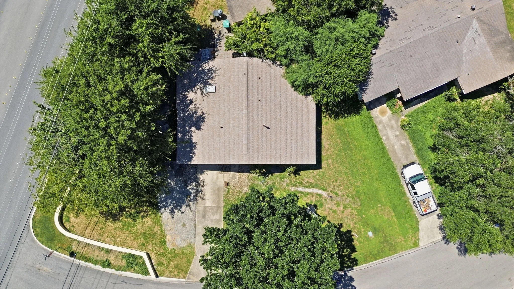 Bird's-eye aerial view displaying the full property layout, driveway, house roof, and surrounding foliage.