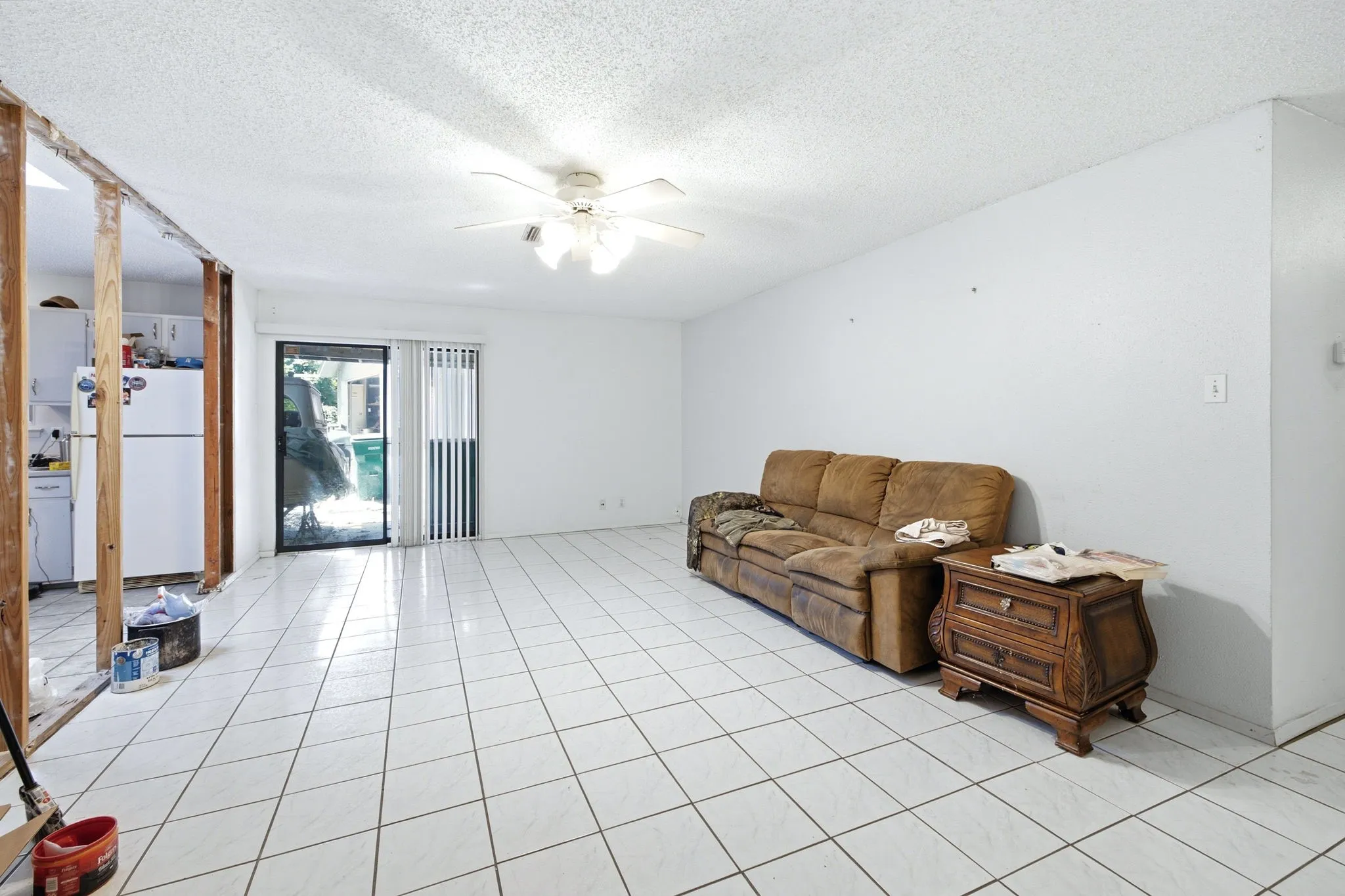 Bright living room featuring white tile flooring, neutral walls, a brown leather sofa, and sliding glass doors.