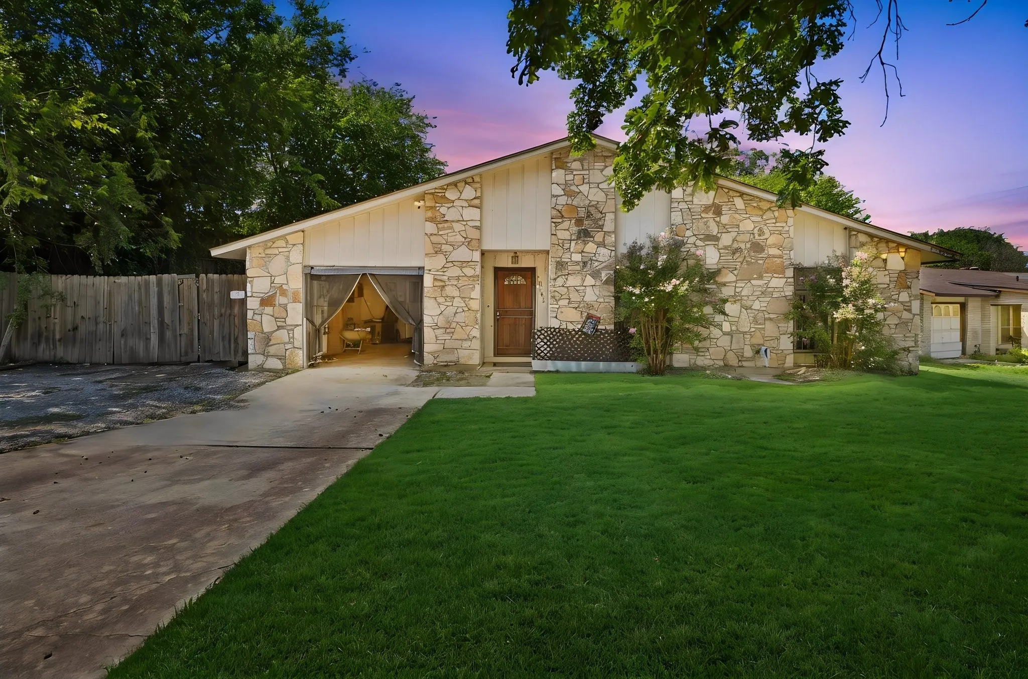 Twilight photo showcasing illuminated windows, double garage, wide concrete driveway, and front lawn.
