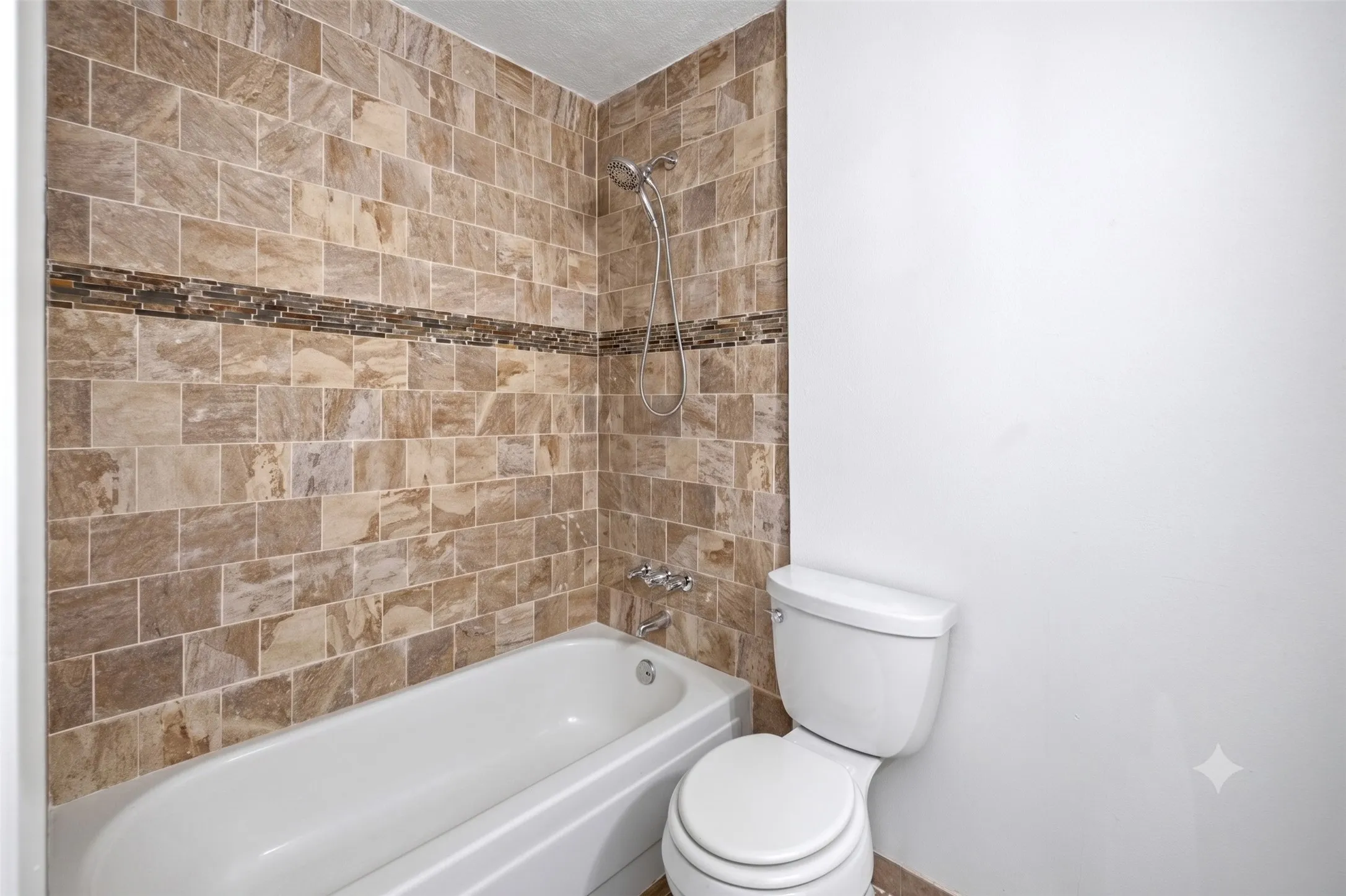Full bathroom equipped with a white bathtub, toilet, and decorative brown tiled surround.
