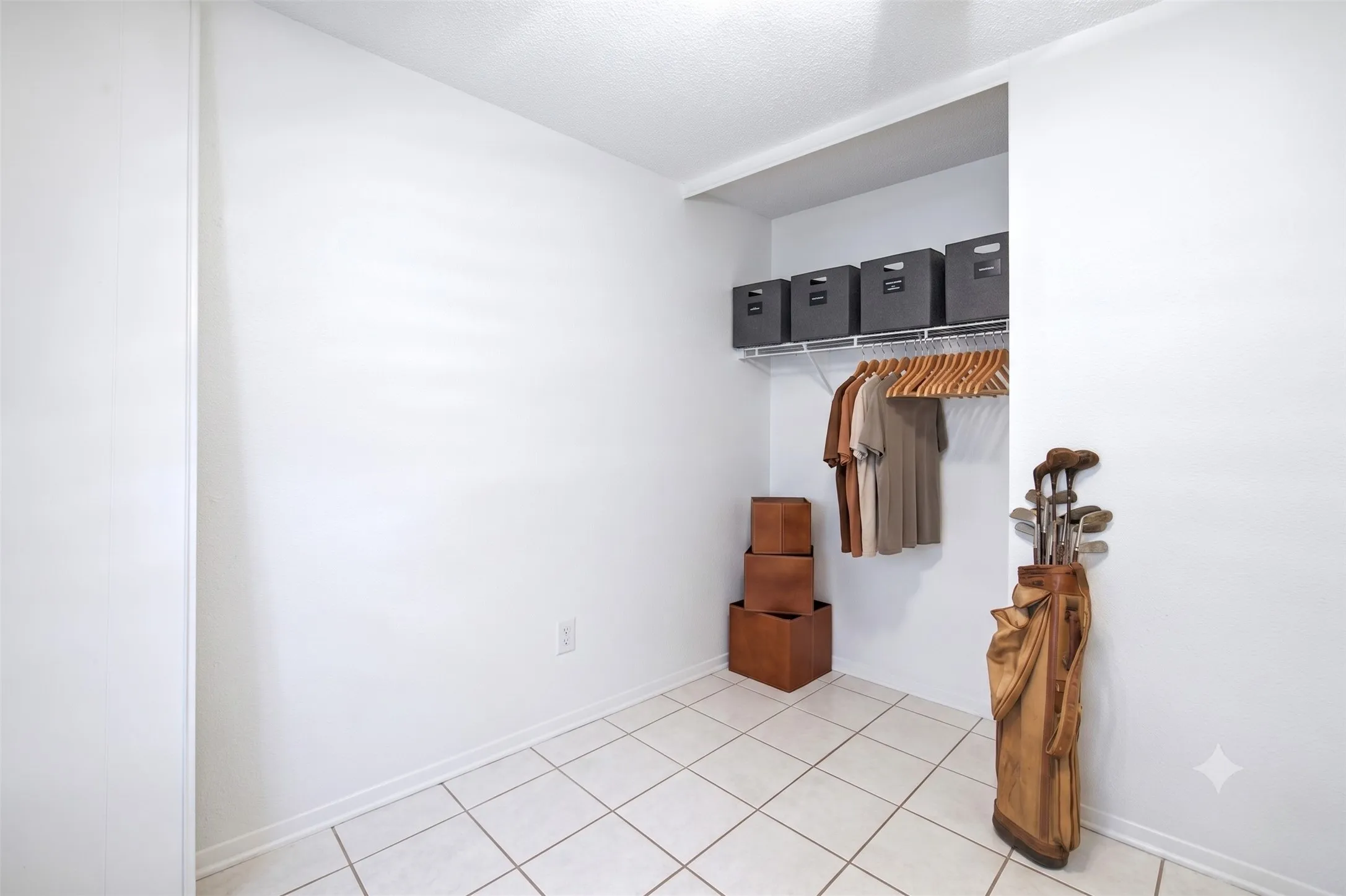 Walk-in closet/storage area with tiled flooring, white walls, built-in shelving, and hanging space.