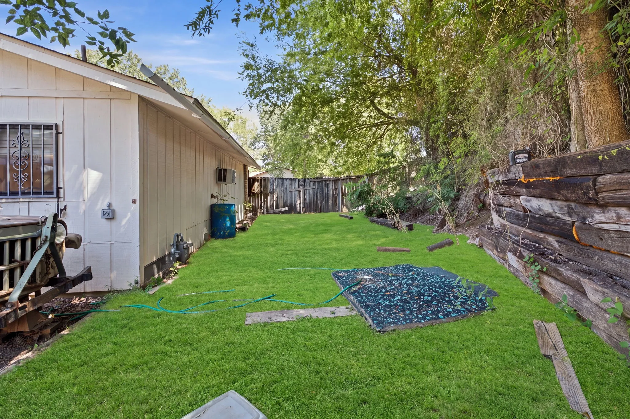 Fenced side yard with lush green grass, mature trees, and the side profile of the home.