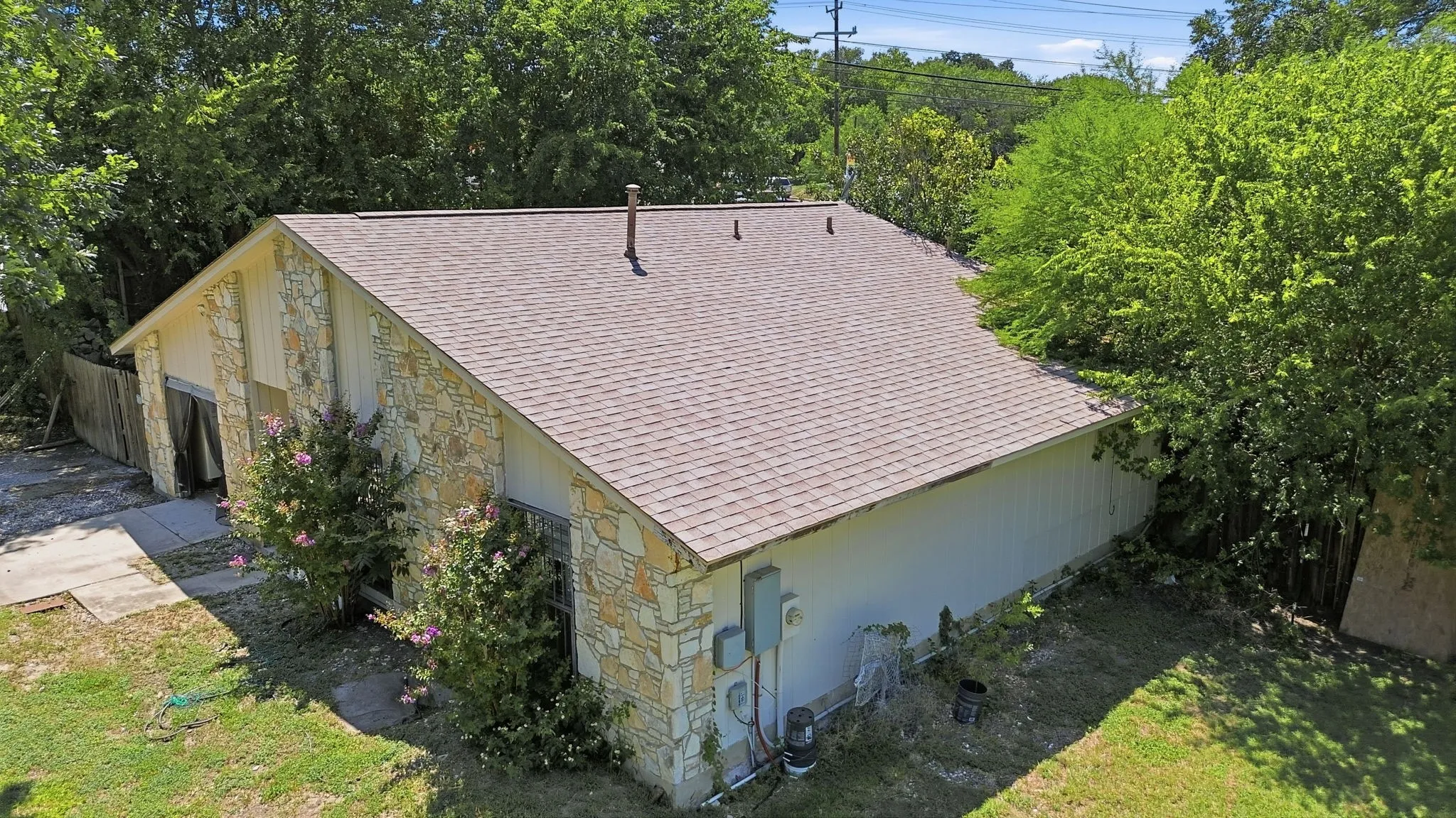 High-angle drone shot showing the rear roofline, exterior stone walls, and surrounding greenery.