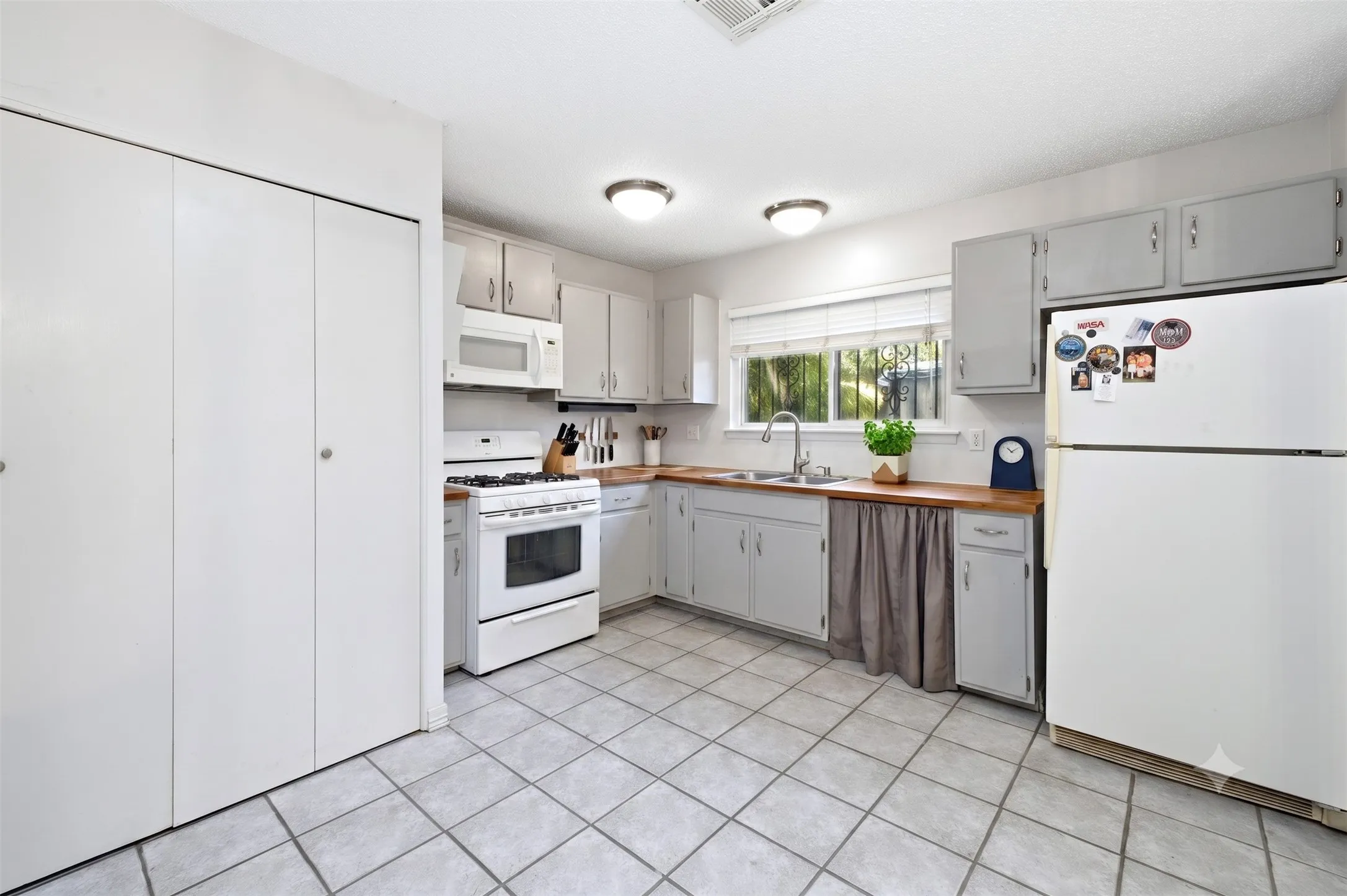Alternate kitchen angle showing white cabinetry, white refrigerator, double sink, and a view into the yard.