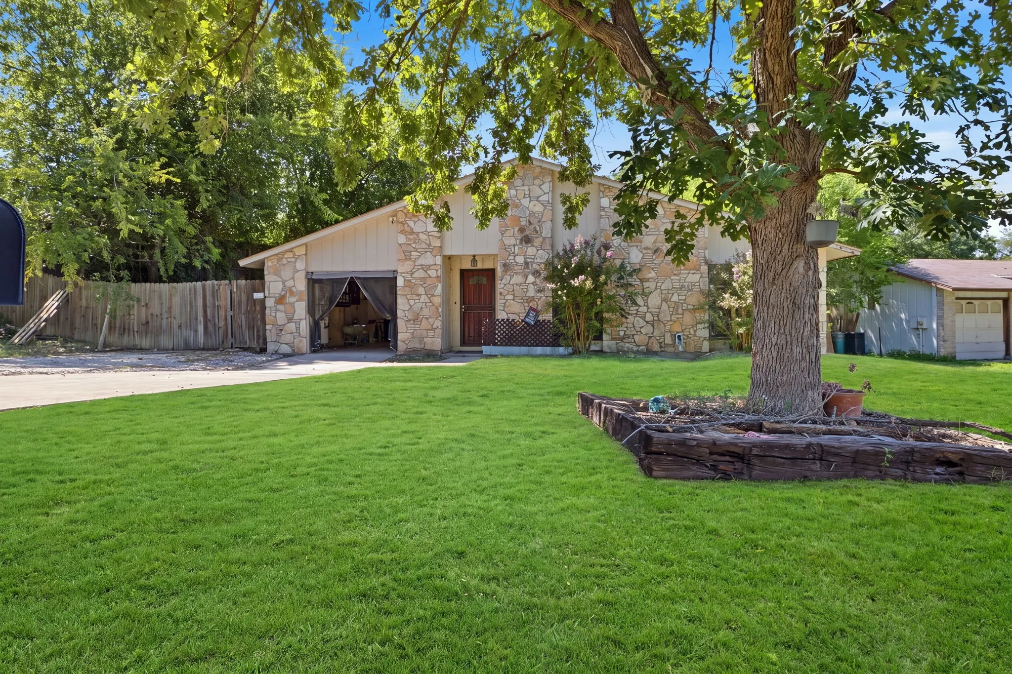 Straight-on front view showing the stone home with double garage doors, framing trees, and a neat lawn.