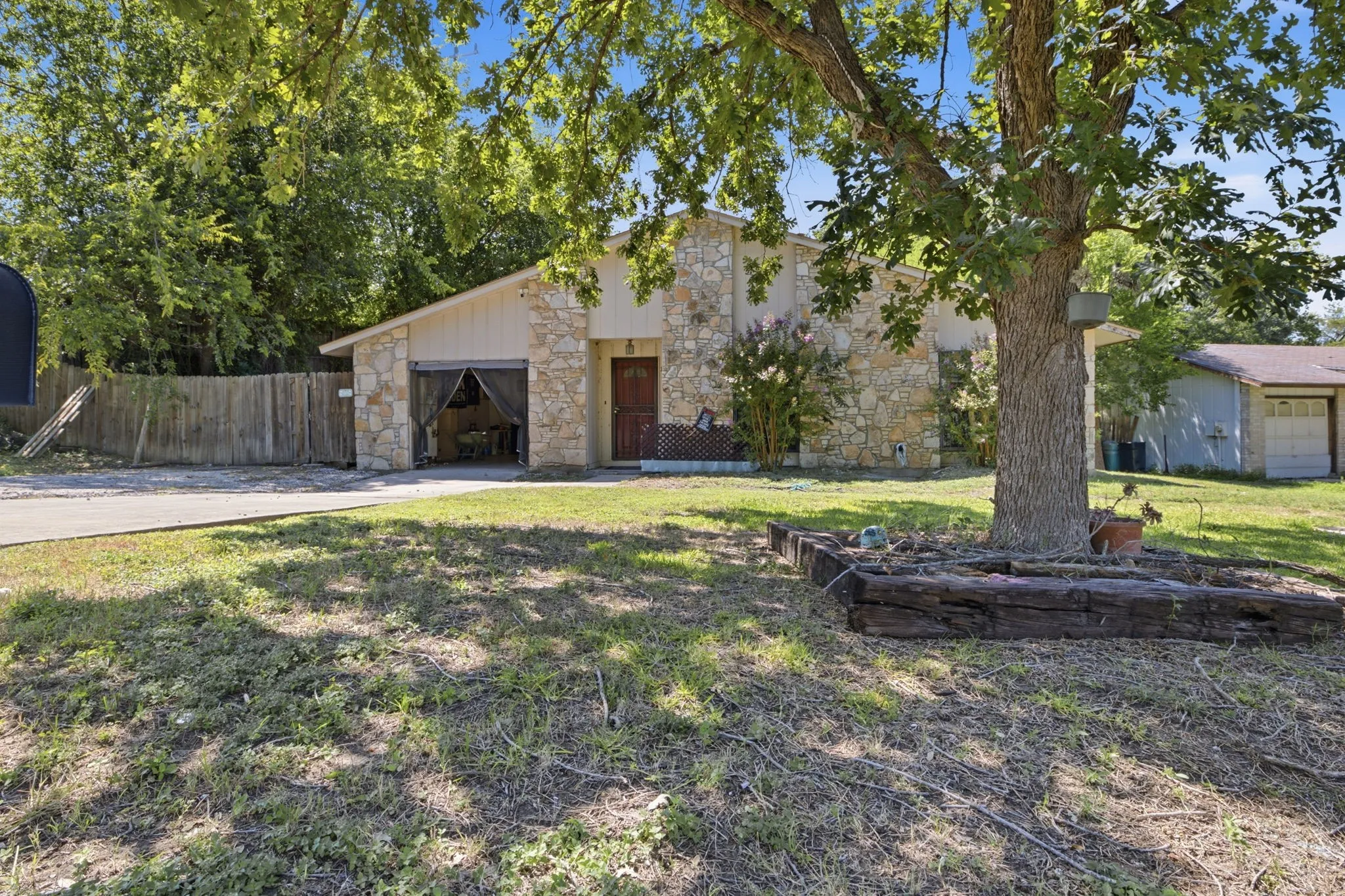 Exterior front view showing the stone house nestled behind large mature trees and a green lawn.