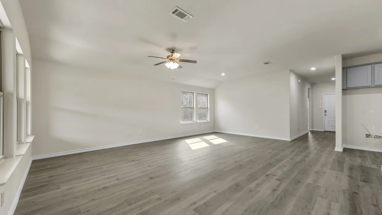 Spacious open-concept living area showcasing gleaming wood-finish flooring throughout, abundant natural light from multiple windows, ceiling fan with integrated lighting, and clean white walls providing a neutral canvas for personalization