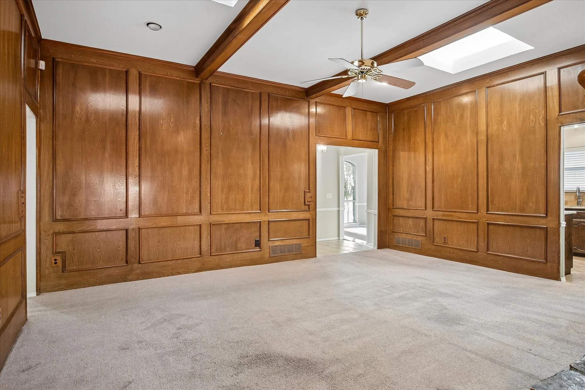 Primary living room with wonderful wood paneling, beams and skylights. Opens to the bedrooms on the left, the front entry at center, kitchen to right, and secondary living room to the rear of photographer. Fireplace is visible in front right corner of photo.