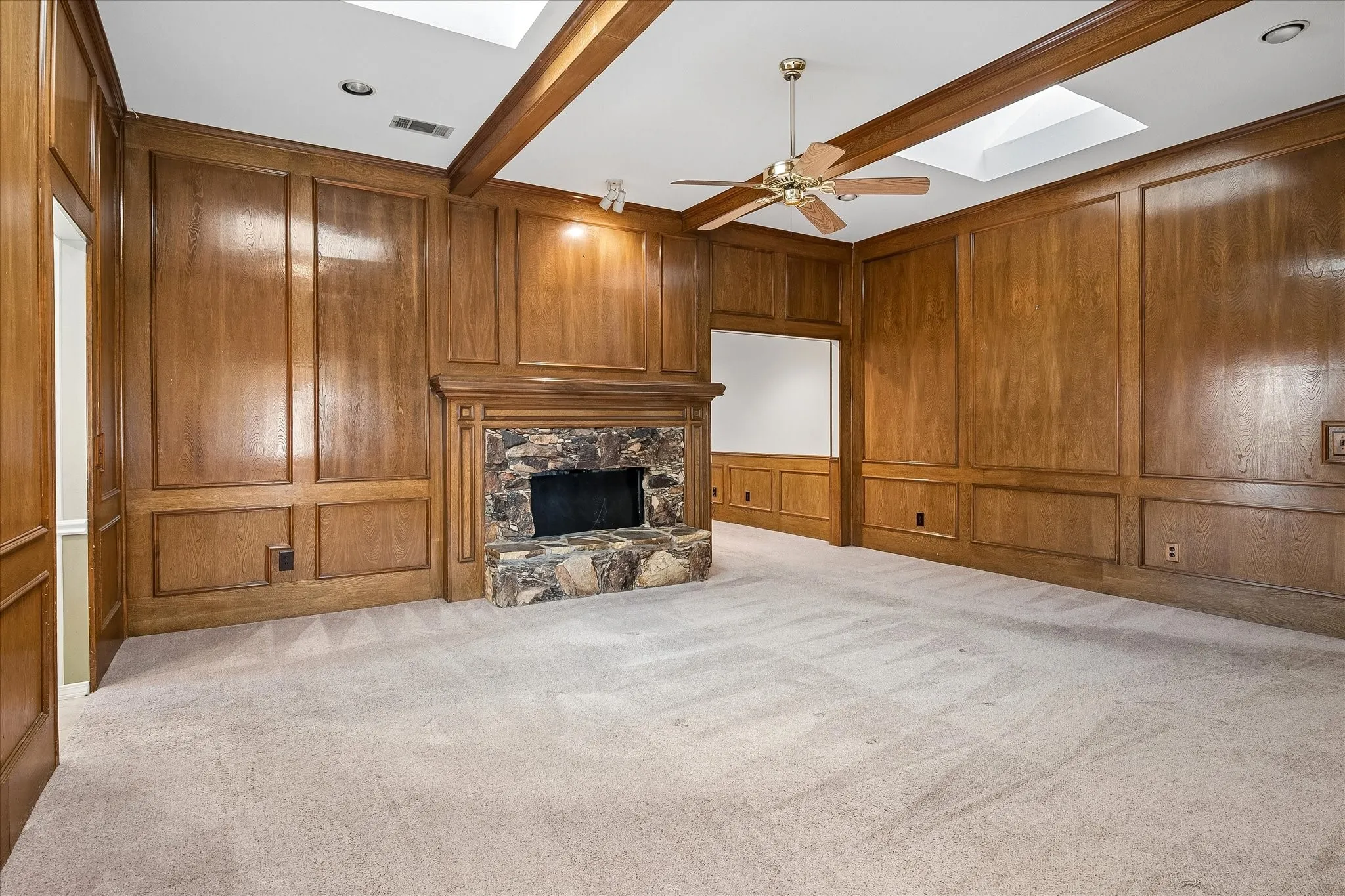 Primary living room with rustic, rock fireplace. This view shows entry to kitchen/breakfast room on left, and threshold to secondary living room at center. Front entry is behind the photographer.