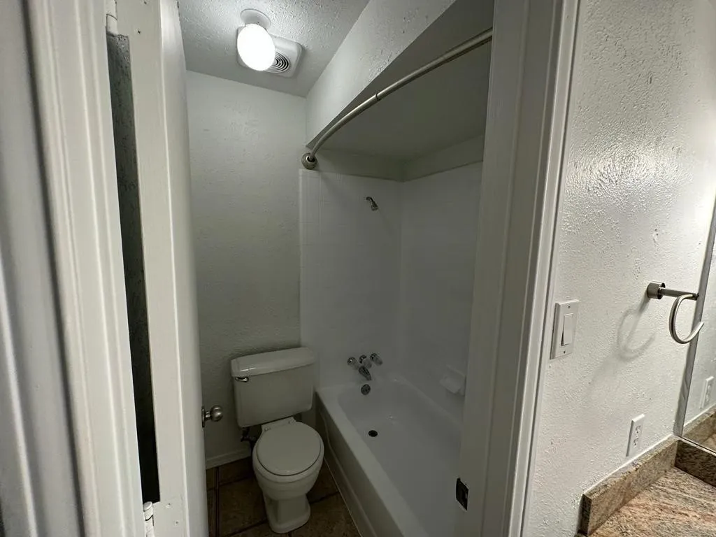 Full bathroom with a white tub and shower combination, a white toilet, and a vanity with a stone-finish countertop