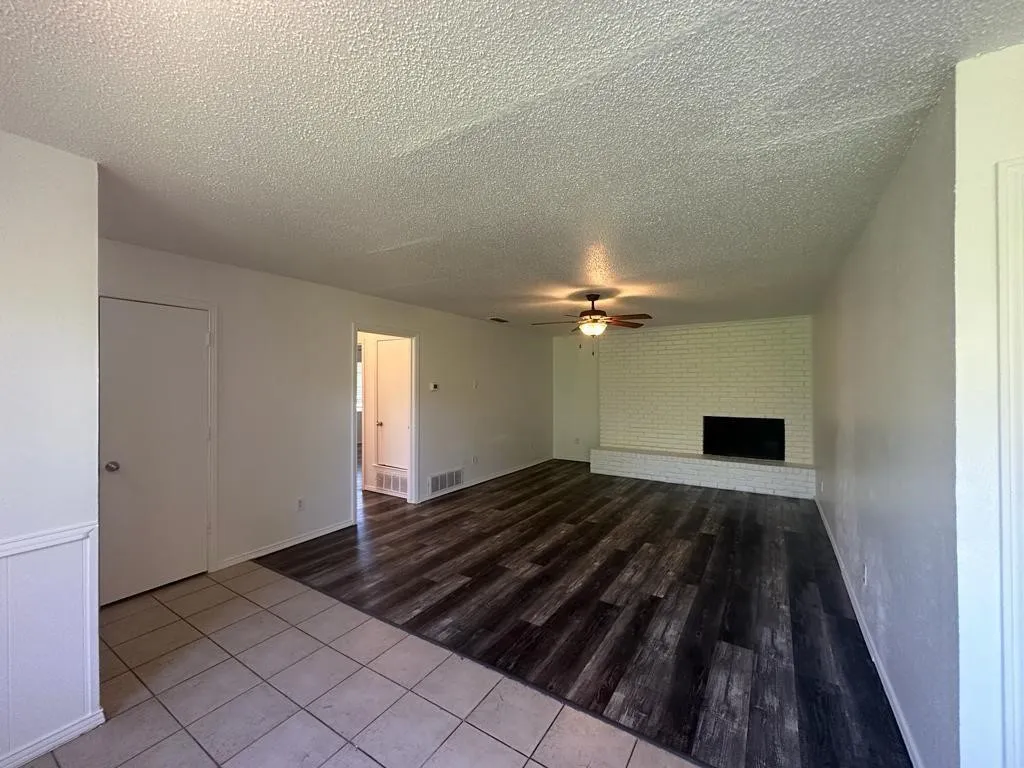 Spacious living area showcasing wood-finish flooring, ceiling fan with integrated lighting, and a fireplace with black surround