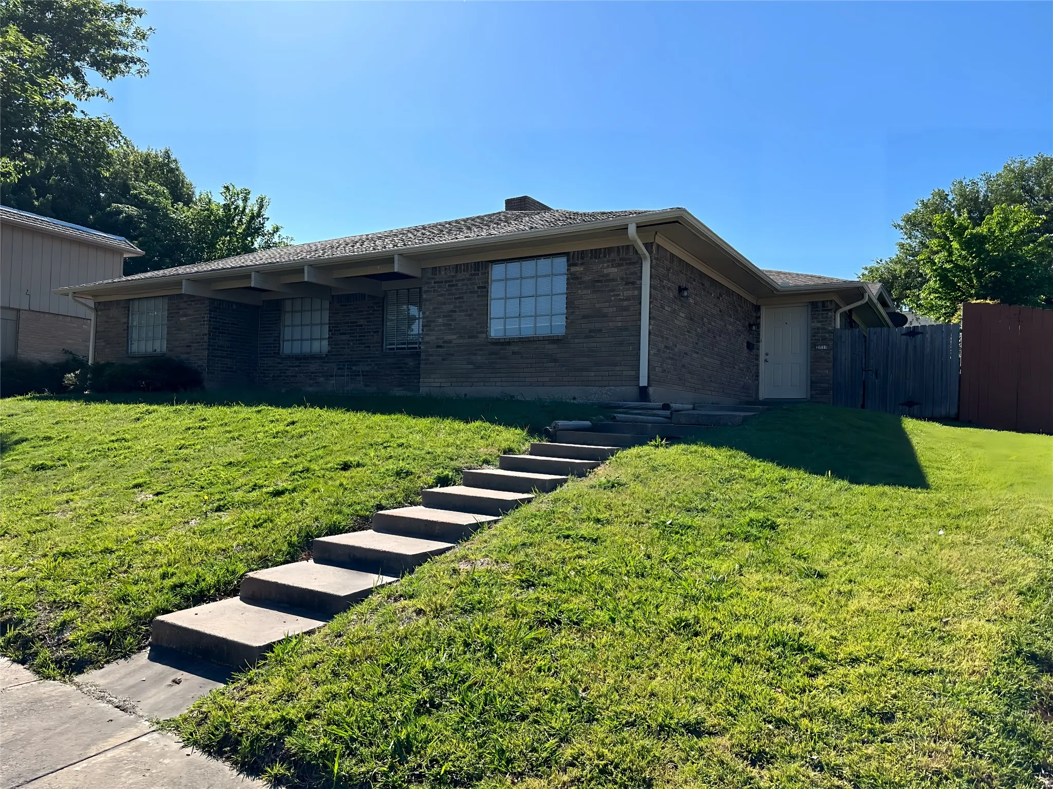 Brick exterior residence featuring a front door, multiple windows, a sloped lawn, and concrete steps leading to the entrance
