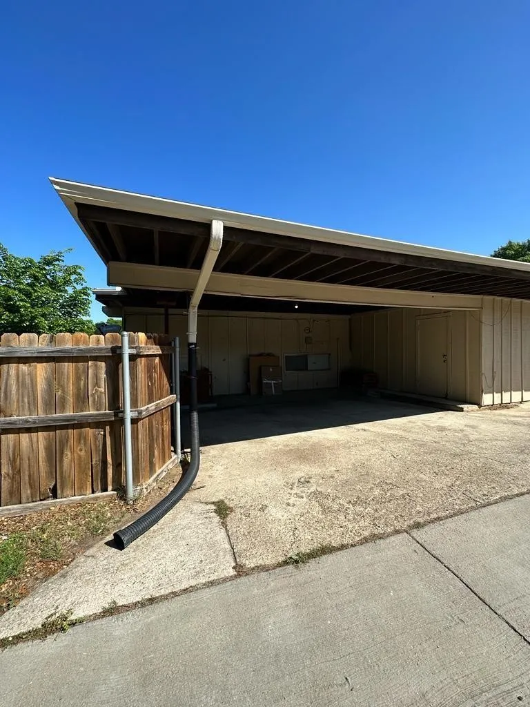 Covered carport with concrete flooring, wood soffit, and exposed rafter tails