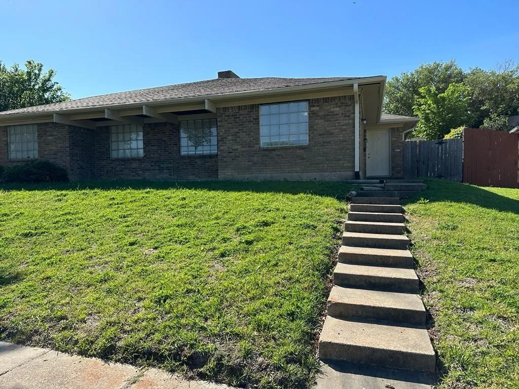 Brick ranch home with manicured lawn, mature landscaping, and defined concrete walkway leading to the front entrance