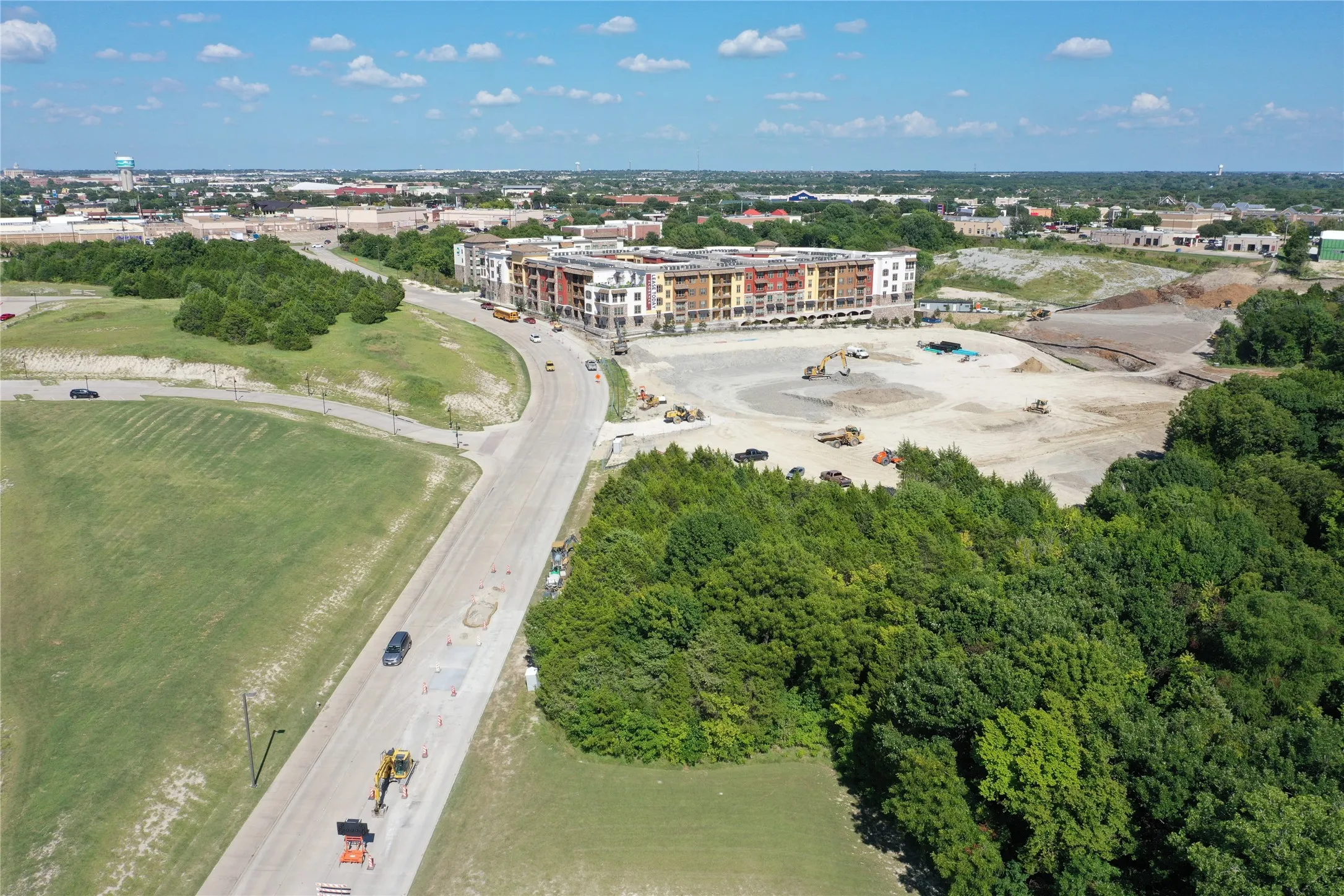 Modern multi-story residential complex featuring contemporary red brick and metal accents, situated on expansive grounds with mature tree lines bordering the property