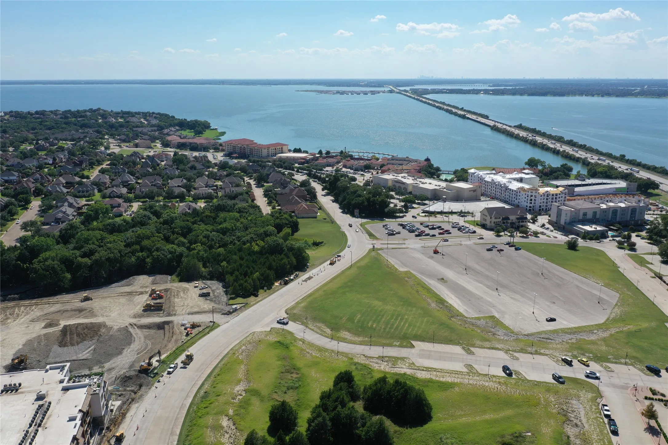 Expansive aerial perspective showcasing manicured lawn grounds, mature tree-lined landscaping, curved driveway with parking areas, and waterfront proximity