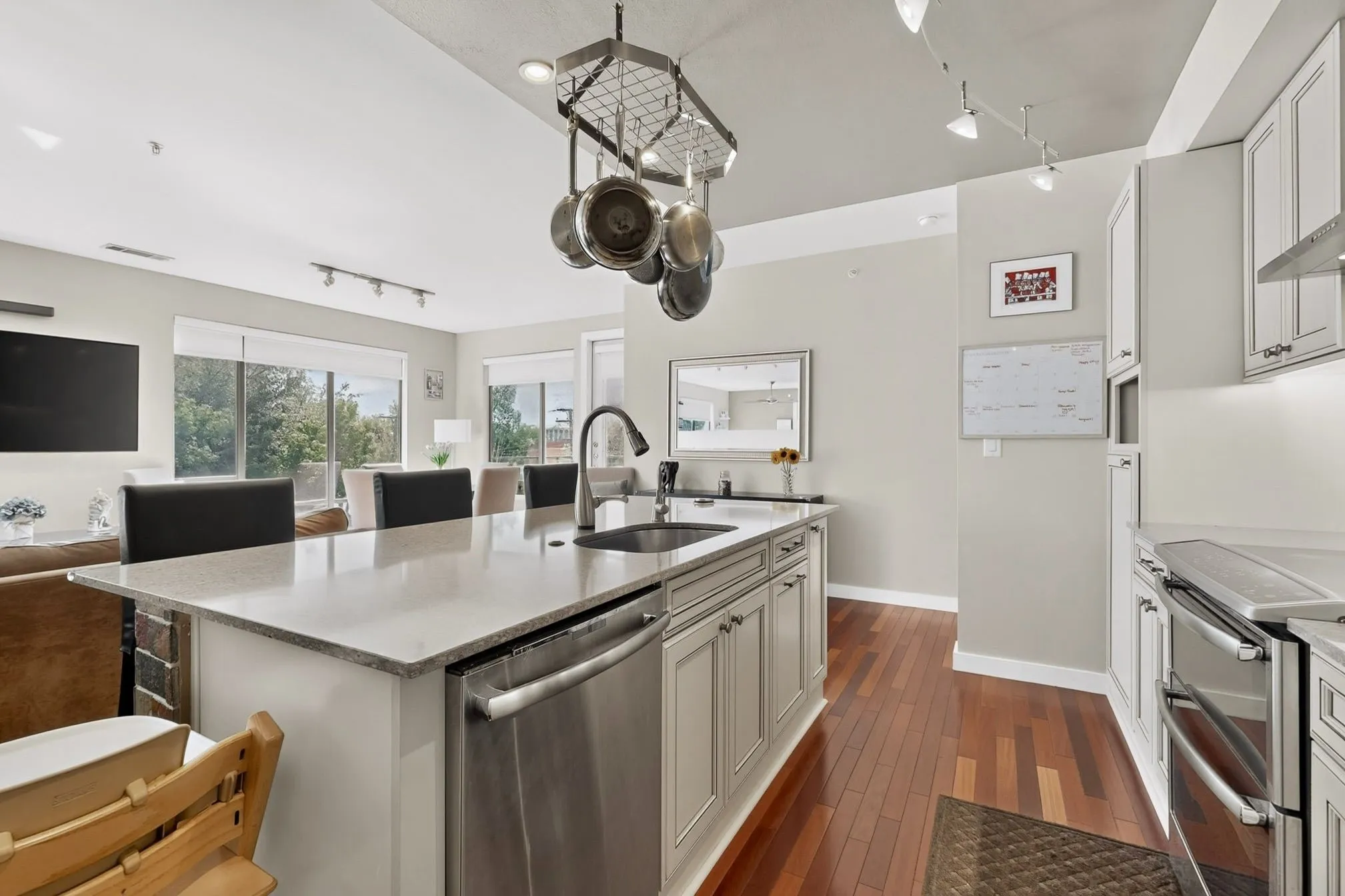 Modern kitchen featuring an island with integrated sink and dishwasher, stainless steel appliances, light-toned cabinetry, and wood-finish flooring throughout