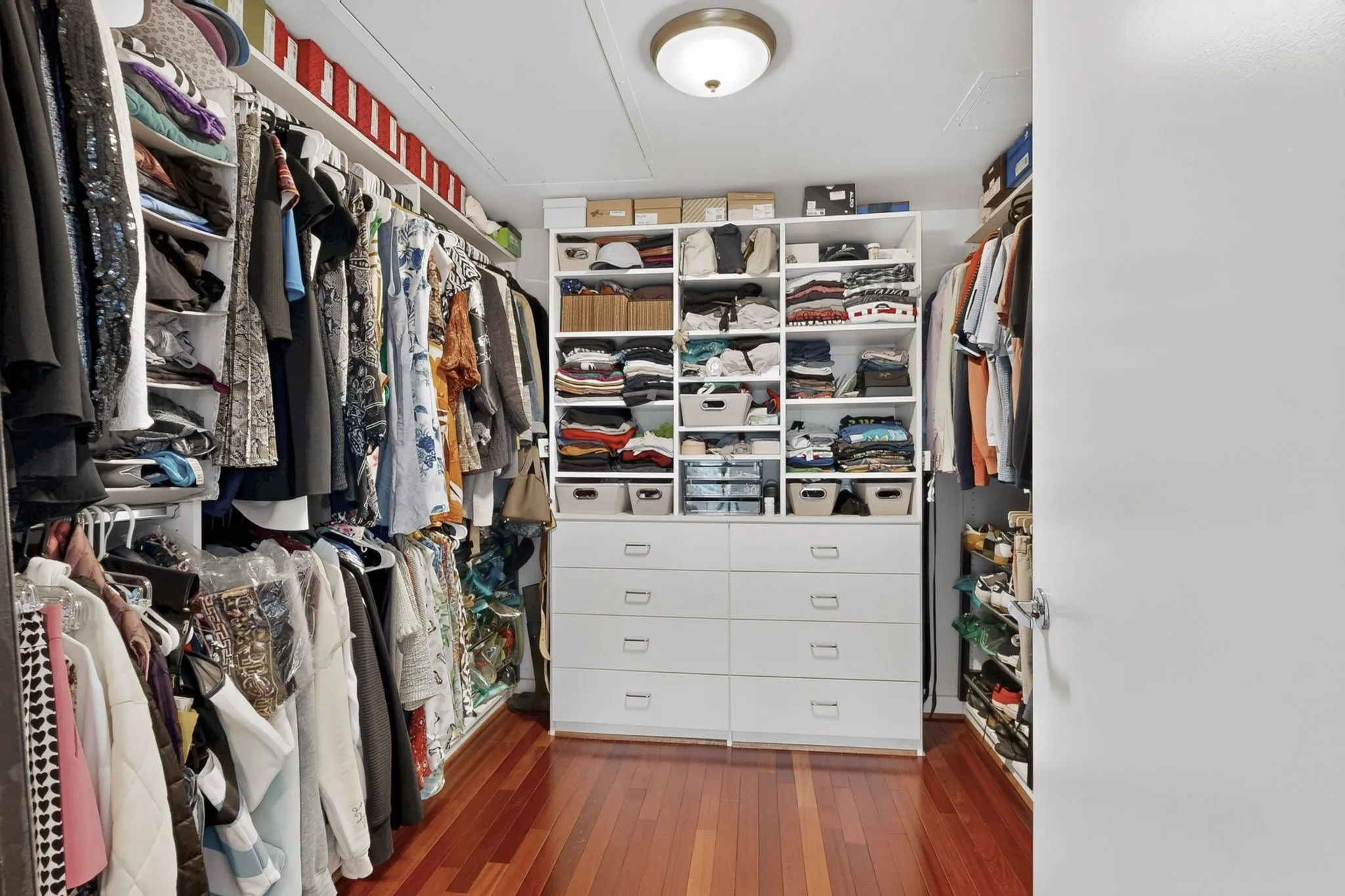 Custom closet system featuring rich wood-finish flooring, ample hanging space, integrated shelving, and multiple drawer units
