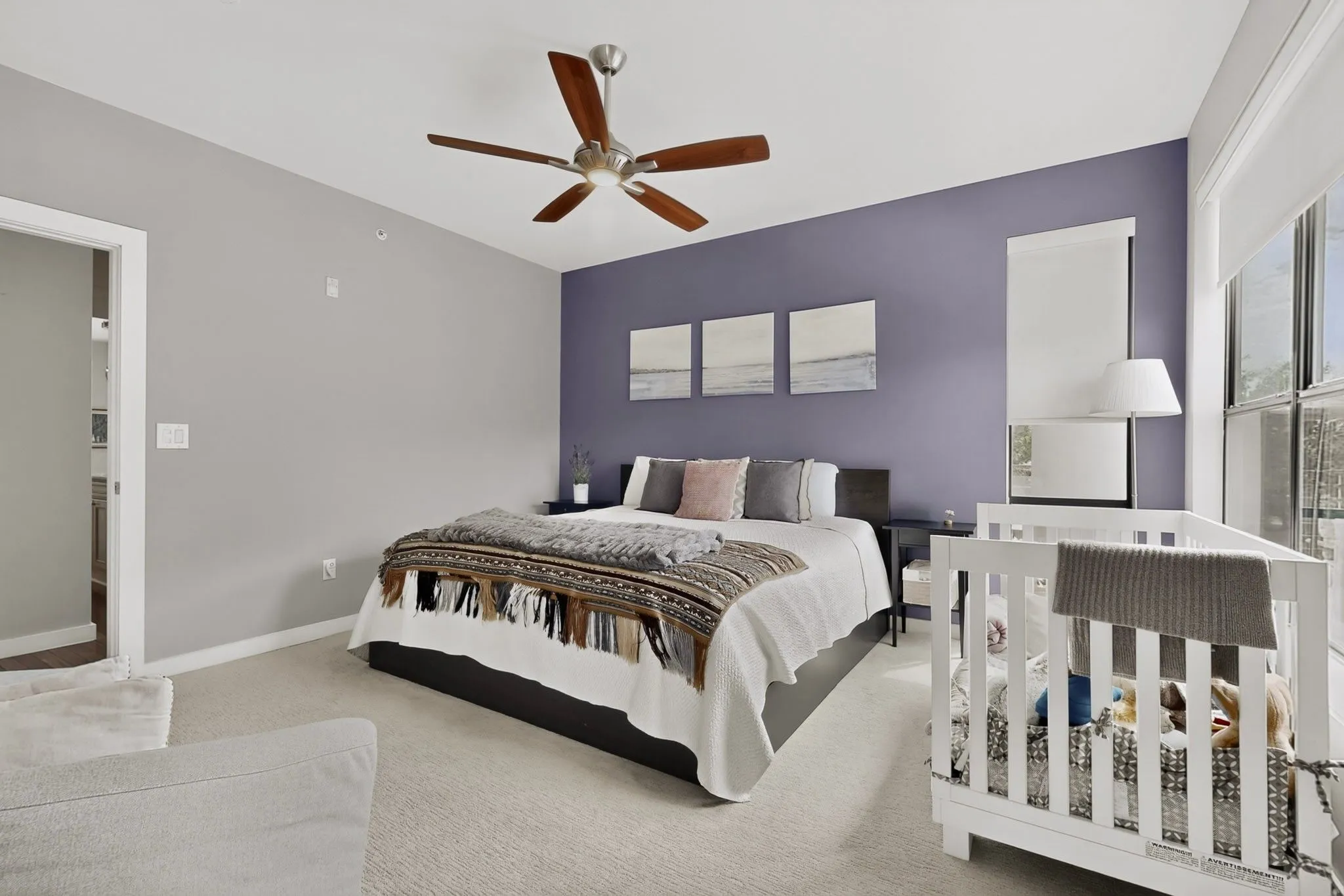 Spacious room featuring carpet flooring, large windows with roller shades, and a ceiling fan with wood-finish blades