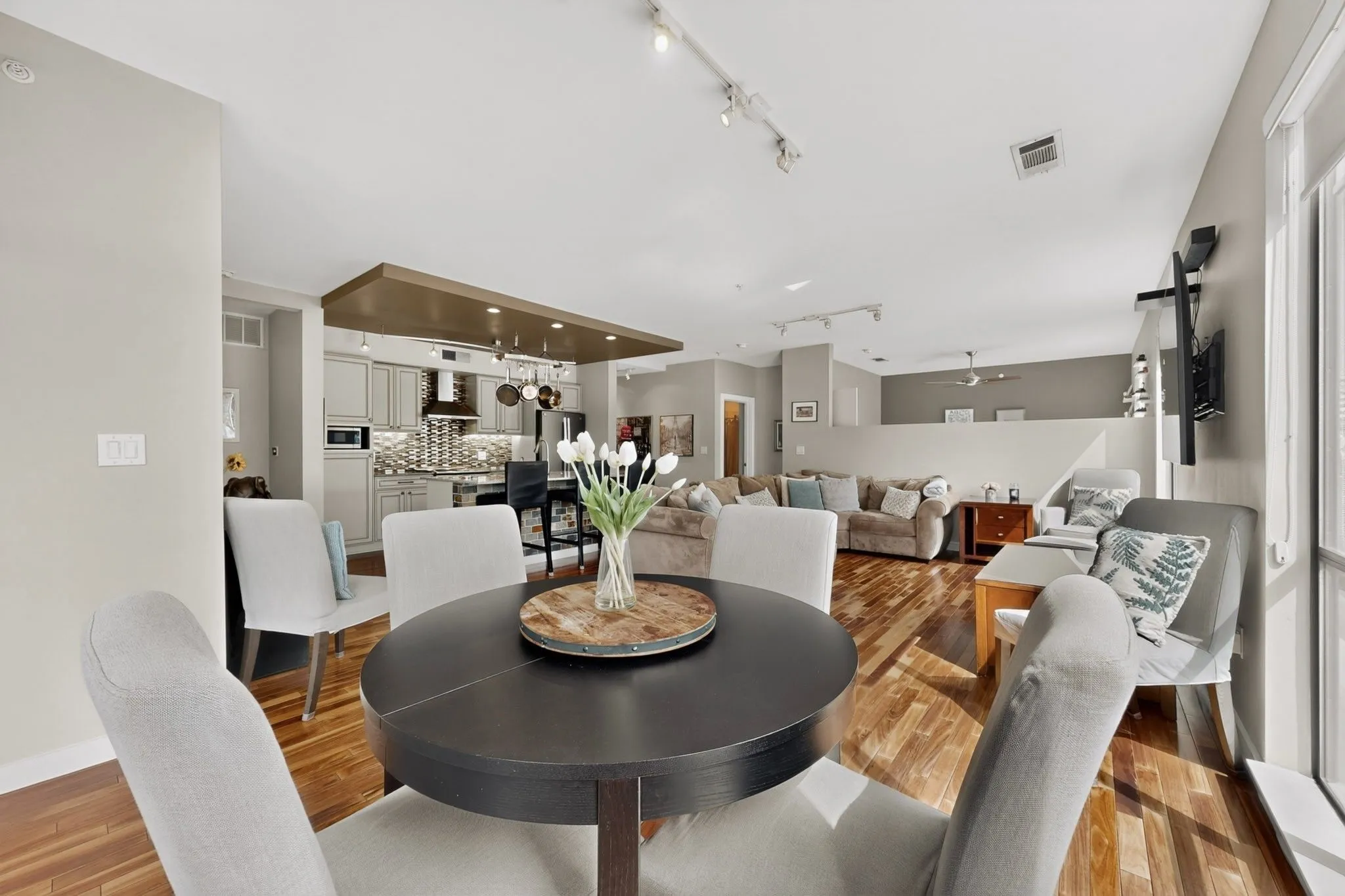 Open-concept living area featuring wood-finish flooring, a contemporary kitchen with light-toned cabinetry and a patterned backsplash, and recessed lighting