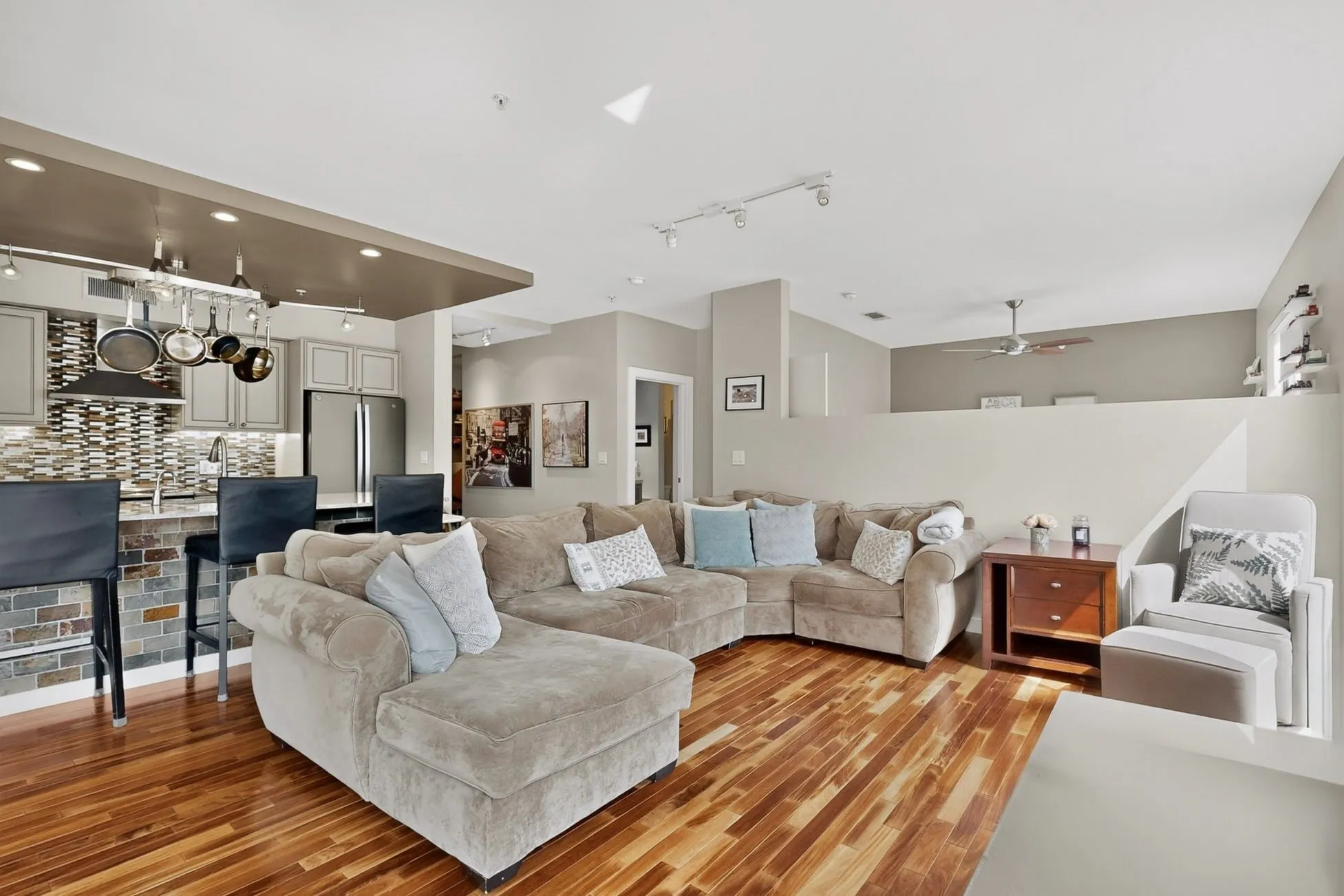 Open-concept living area featuring wood-finish flooring, a kitchen with light gray cabinetry, a multi-tone tile backsplash, and stainless steel appliances