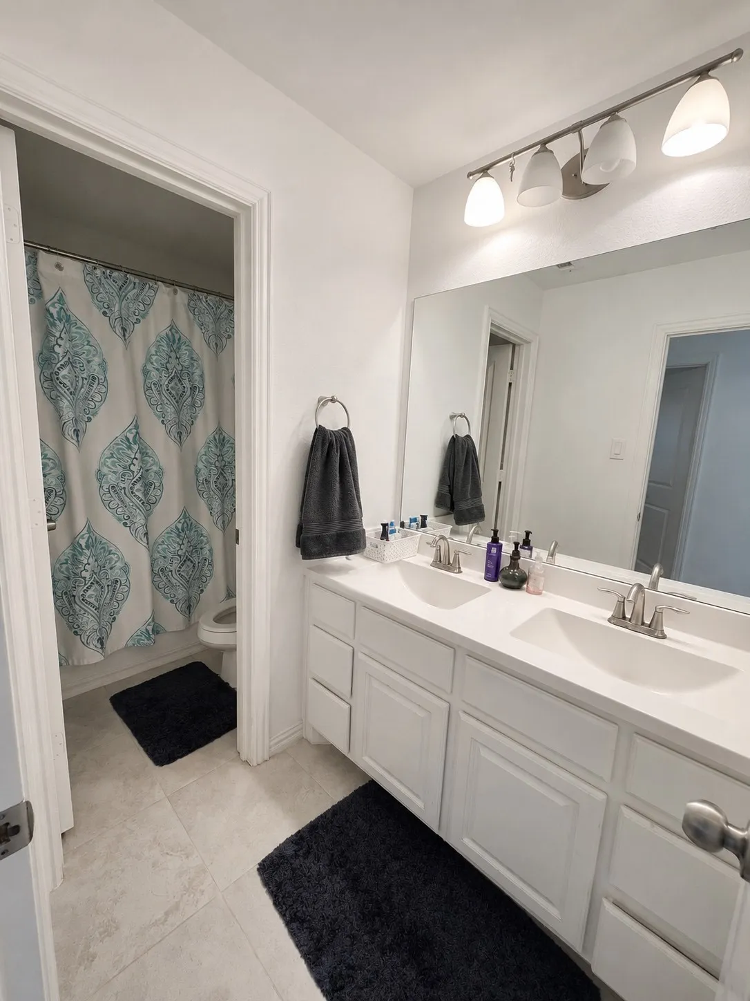 Dual sink vanity with white cabinetry, neutral tile flooring, and overhead track lighting