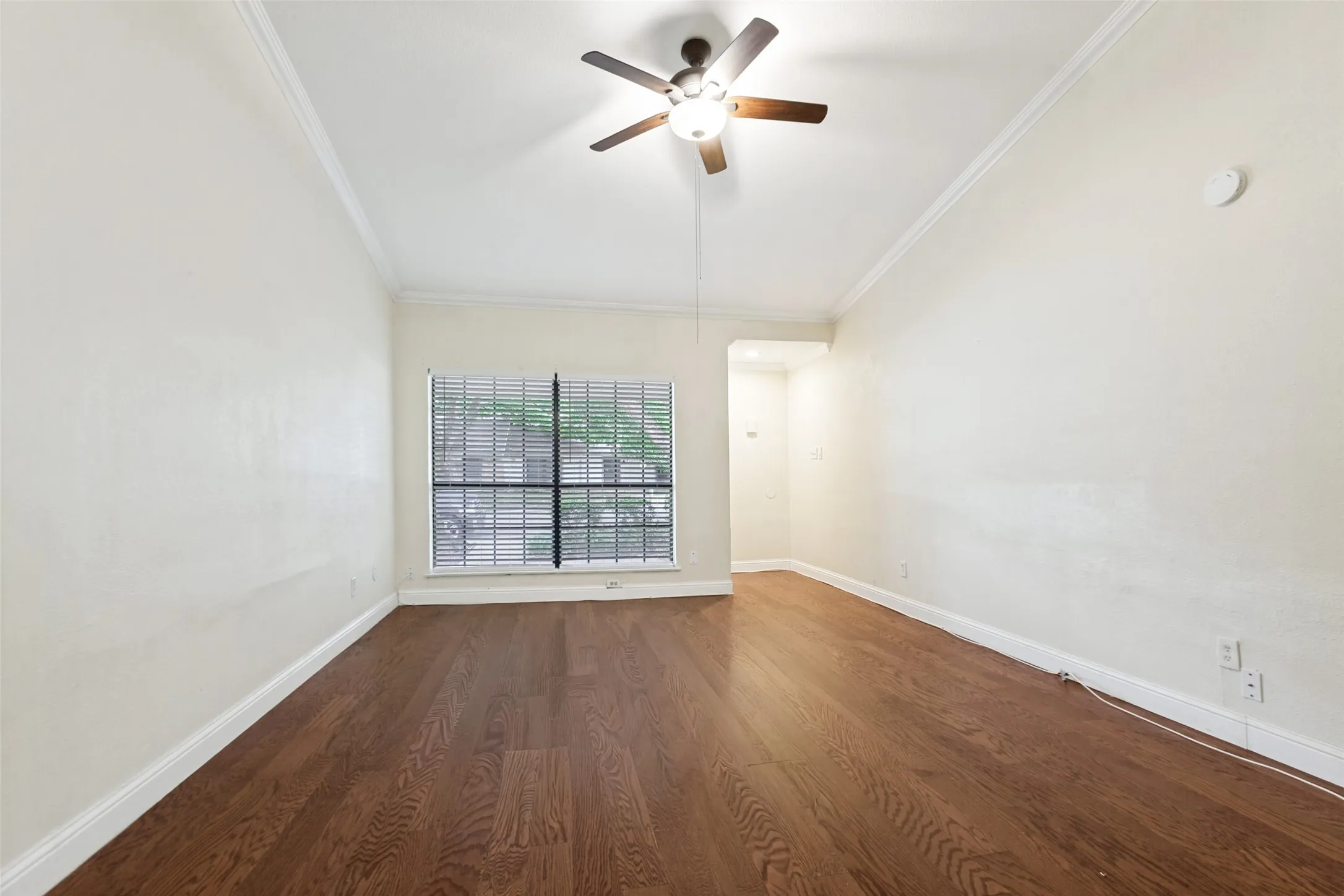 Spacious room featuring wood-finish flooring, white baseboards, and crown molding