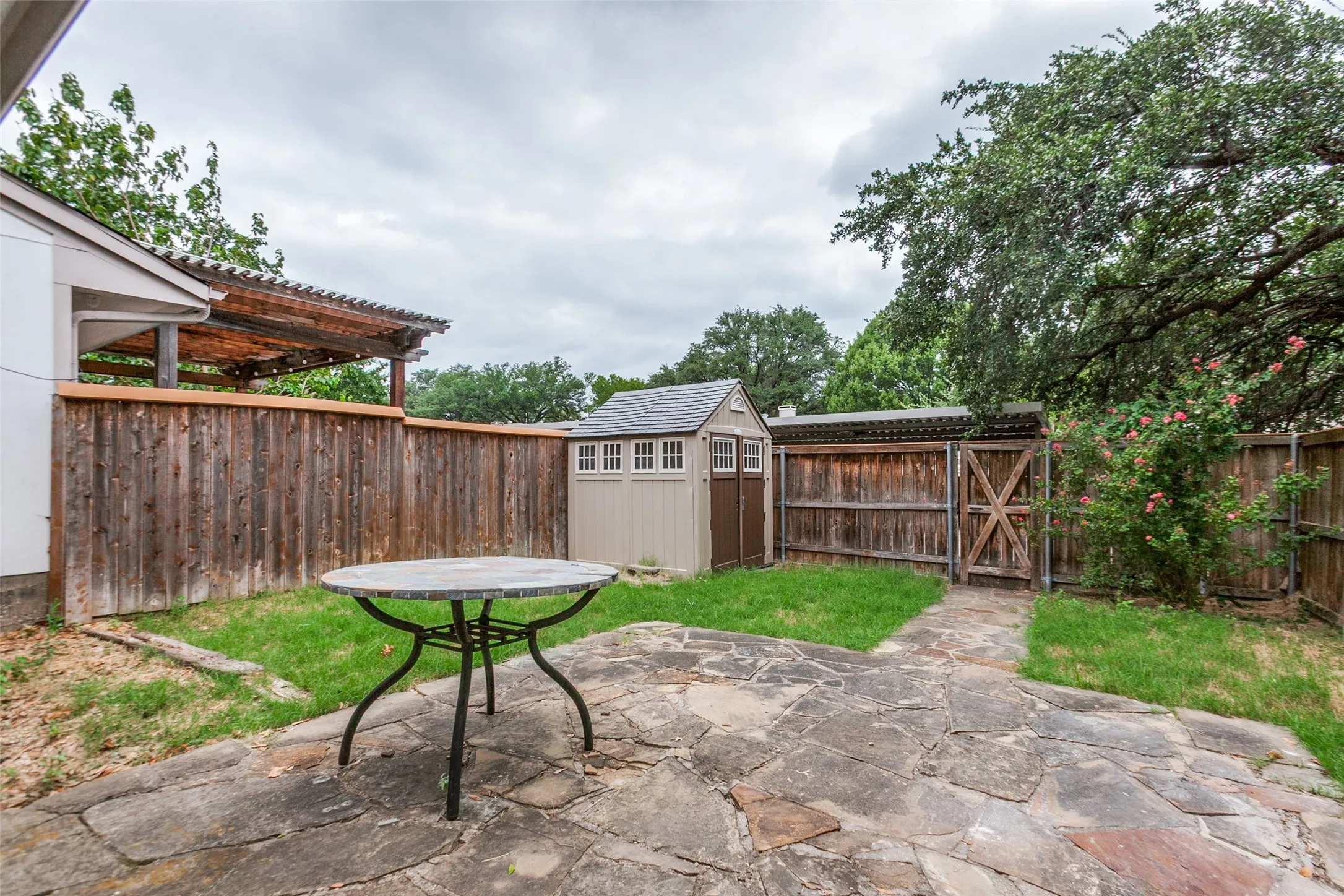 Stone patio with a separate storage shed, privacy fencing, a wooden pergola structure, and a secondary fenced area