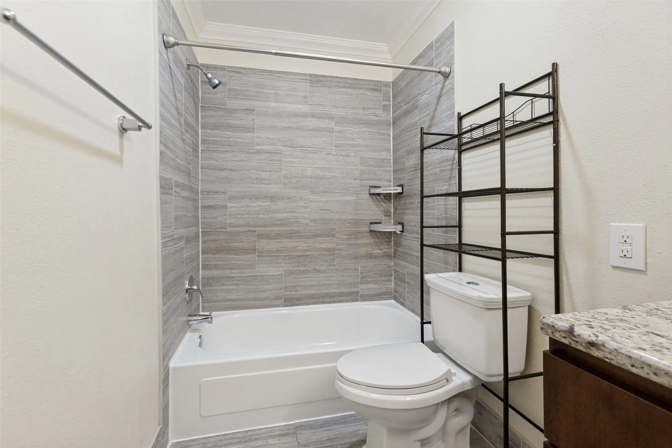 Bathroom featuring a white bathtub, tiled shower surround with built-in shelving, white toilet, and a vanity with a stone countertop