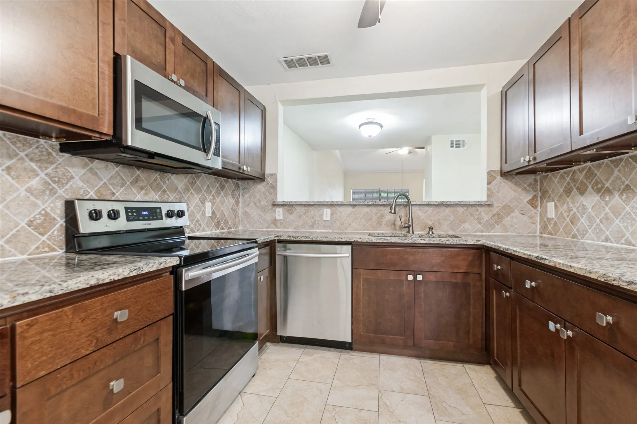Kitchen featuring rich wood cabinetry, granite-style countertops, stainless steel appliances, a tile backsplash, and tile flooring