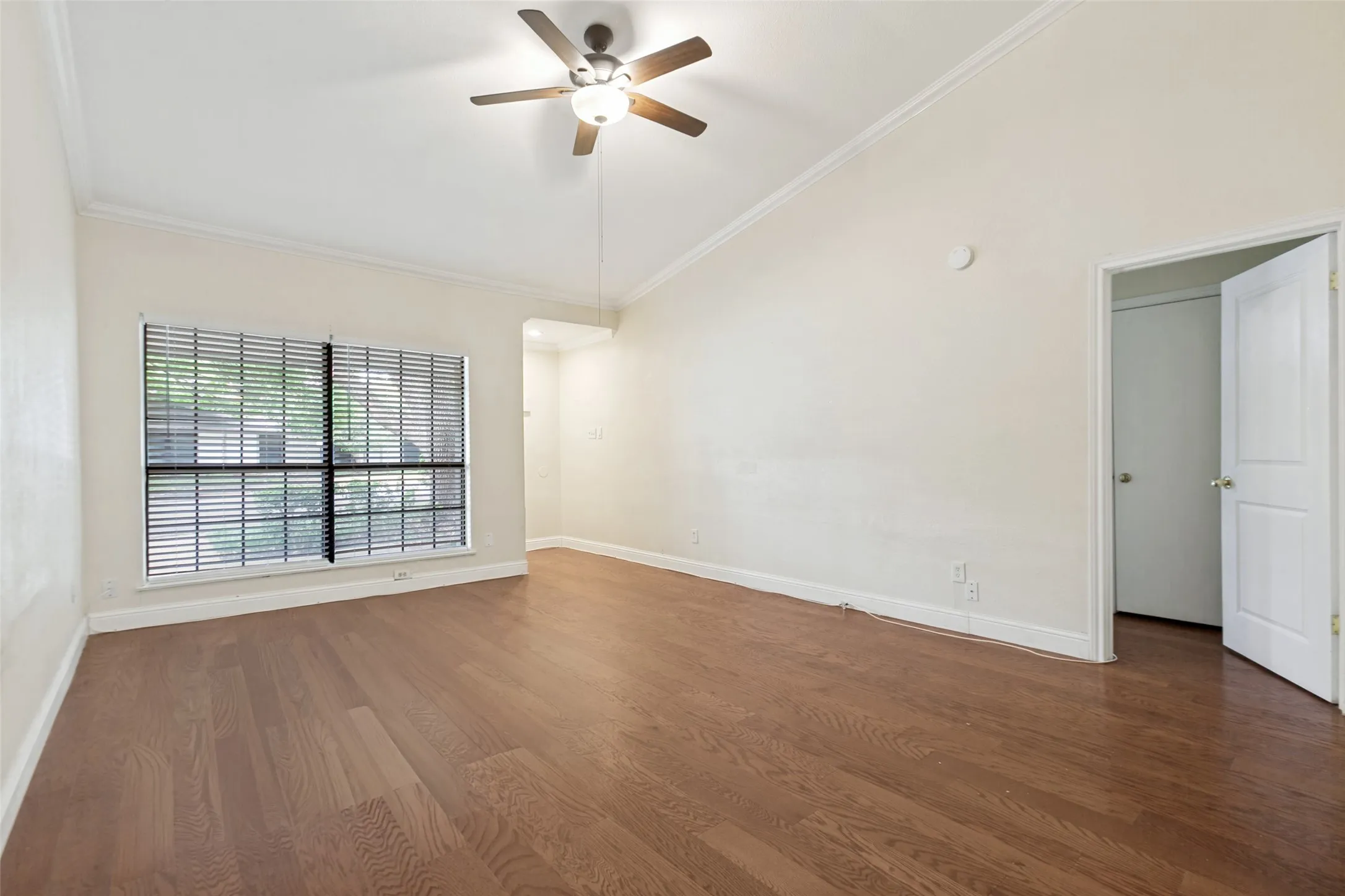 Spacious room featuring wood-finish flooring, a vaulted ceiling, and crown molding