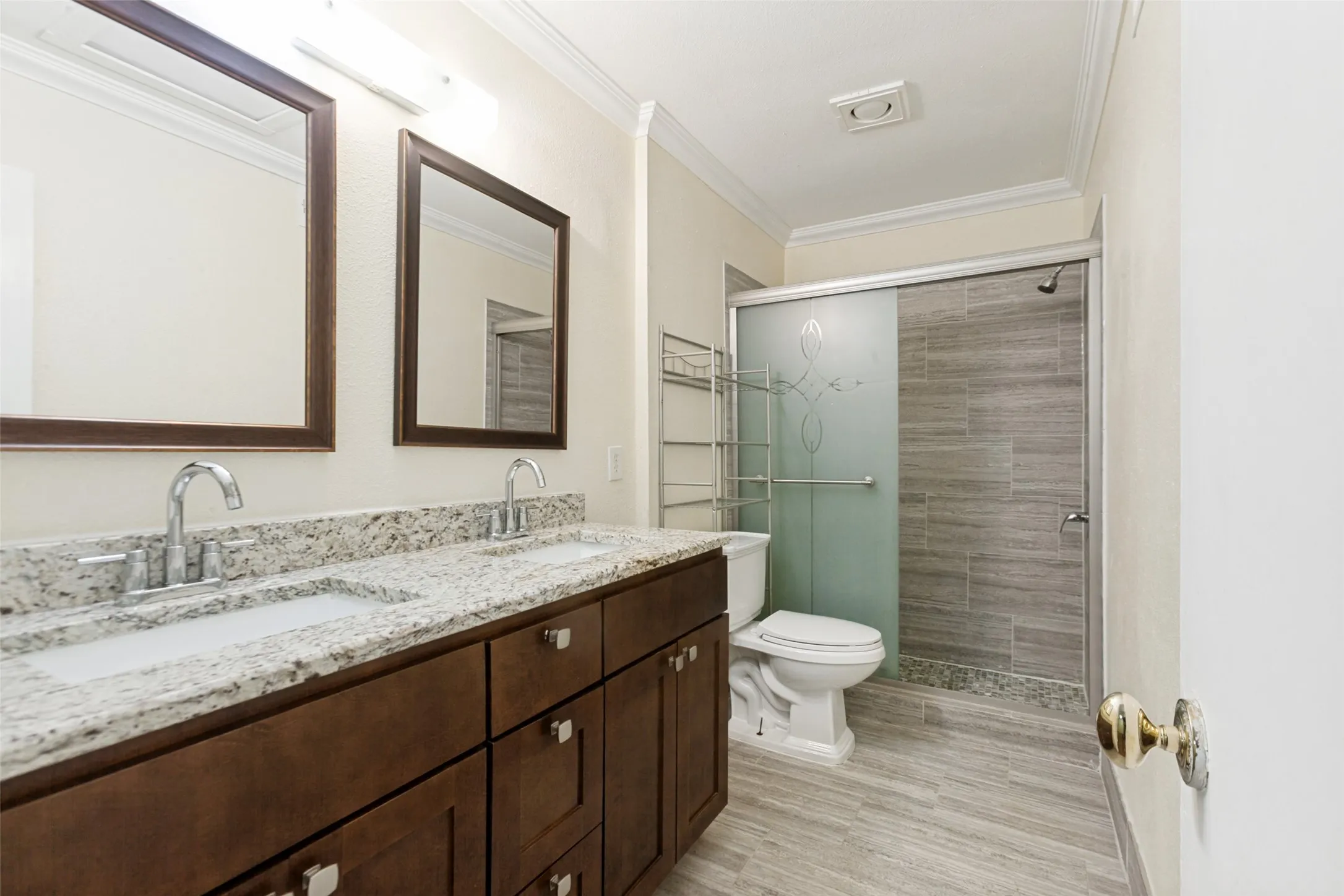 Bathroom featuring a dual vanity with a speckled countertop, brown wood cabinetry, and chrome fixtures