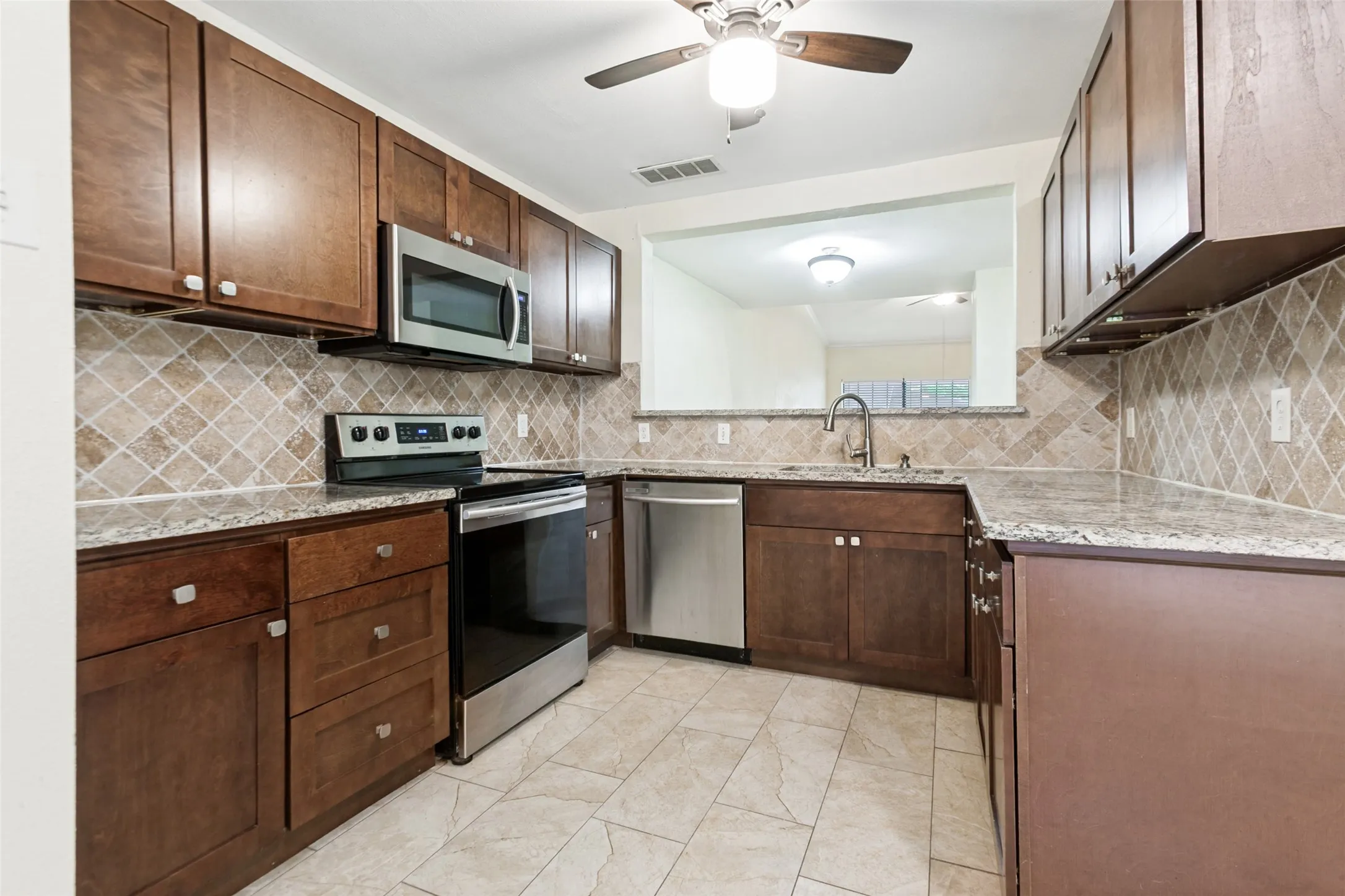 Kitchen featuring wood-finish cabinetry, stainless steel appliances, a tile backsplash, and light-toned flooring