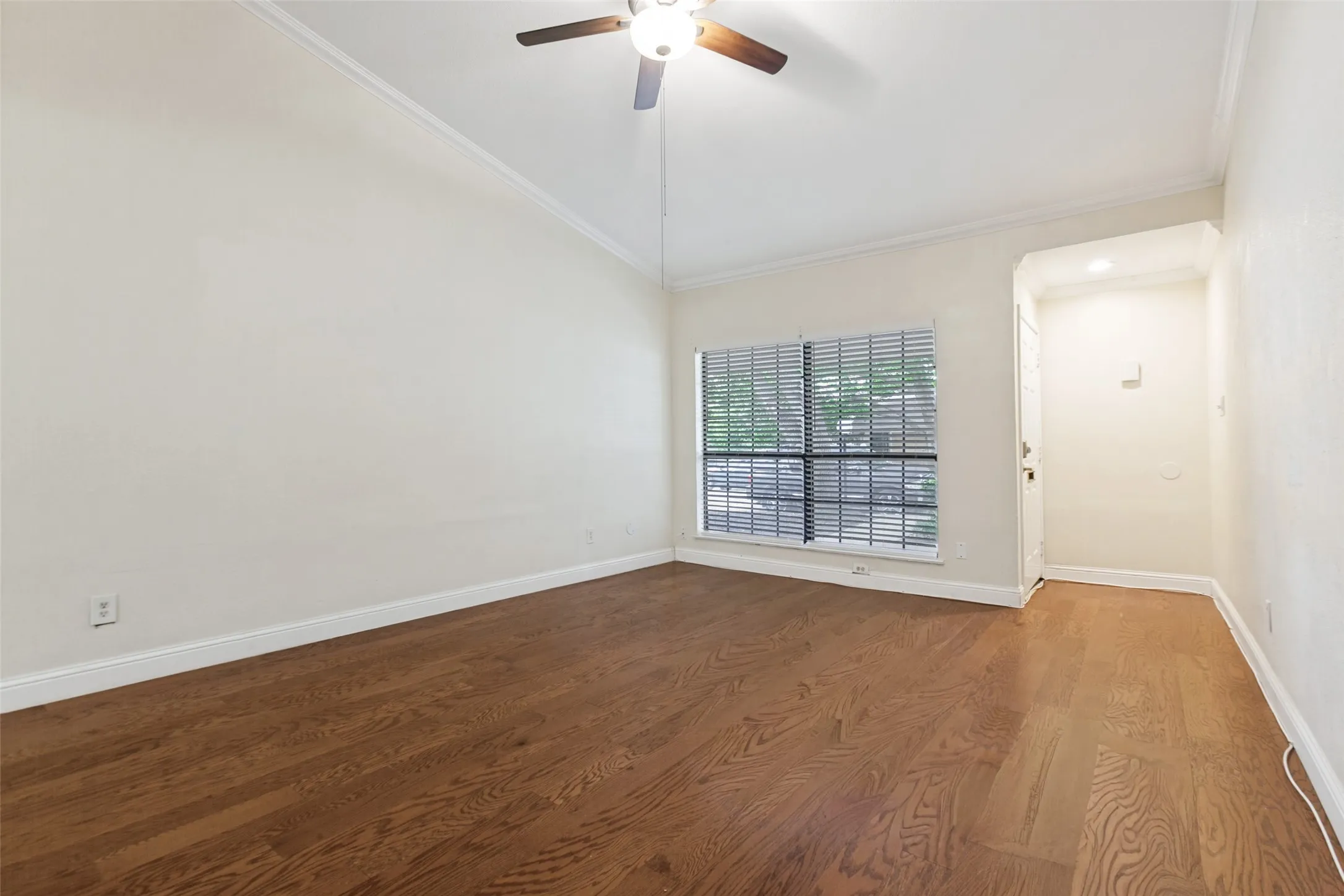 Spacious room featuring rich wood-finish flooring, white walls, and abundant natural light from large windows with blinds